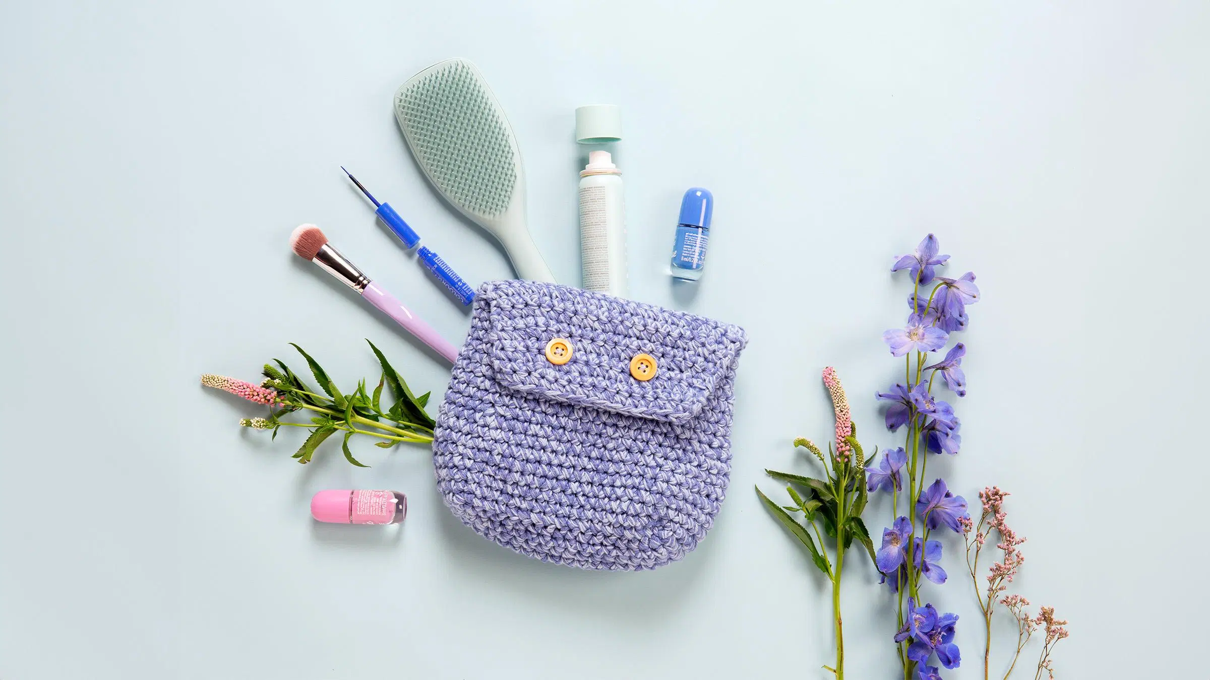Virkattu käsityöpussi, pieniä kauneudenhoitoon liittyviä tavaroita ja kukkia