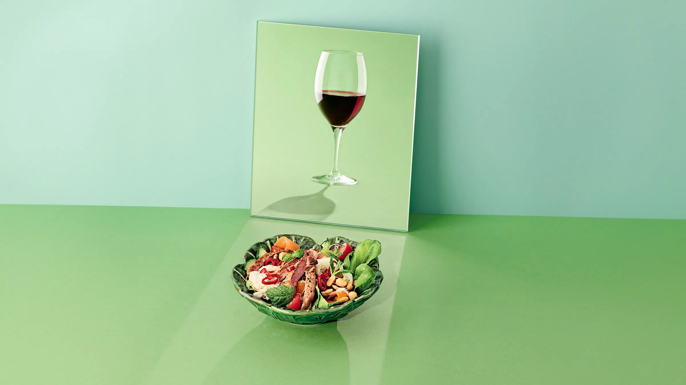 Lautanen, jossa aasialaisittain maustettua pihvisalaattia sekä lasillinen matala-alkokolista punaista viinijuomaa.