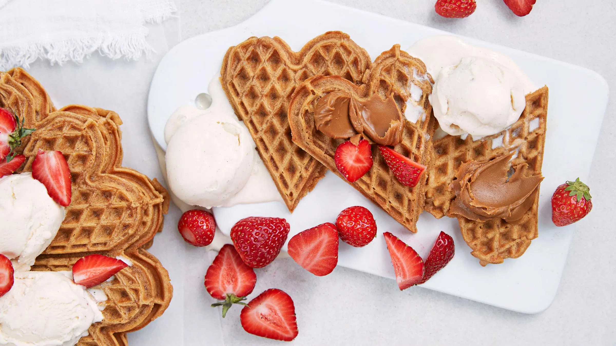 Sydämen muotoisia keksivohveleita, mansikoita ja vaniljajäätelöä.