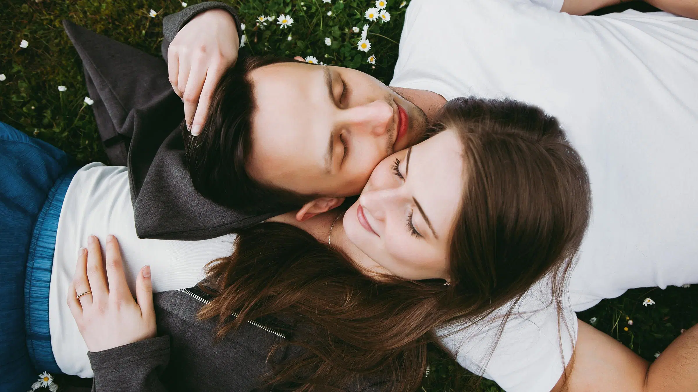 Pariskunta makaa selällään nurmikolla päät toisiaan vasten silmät kiinni.