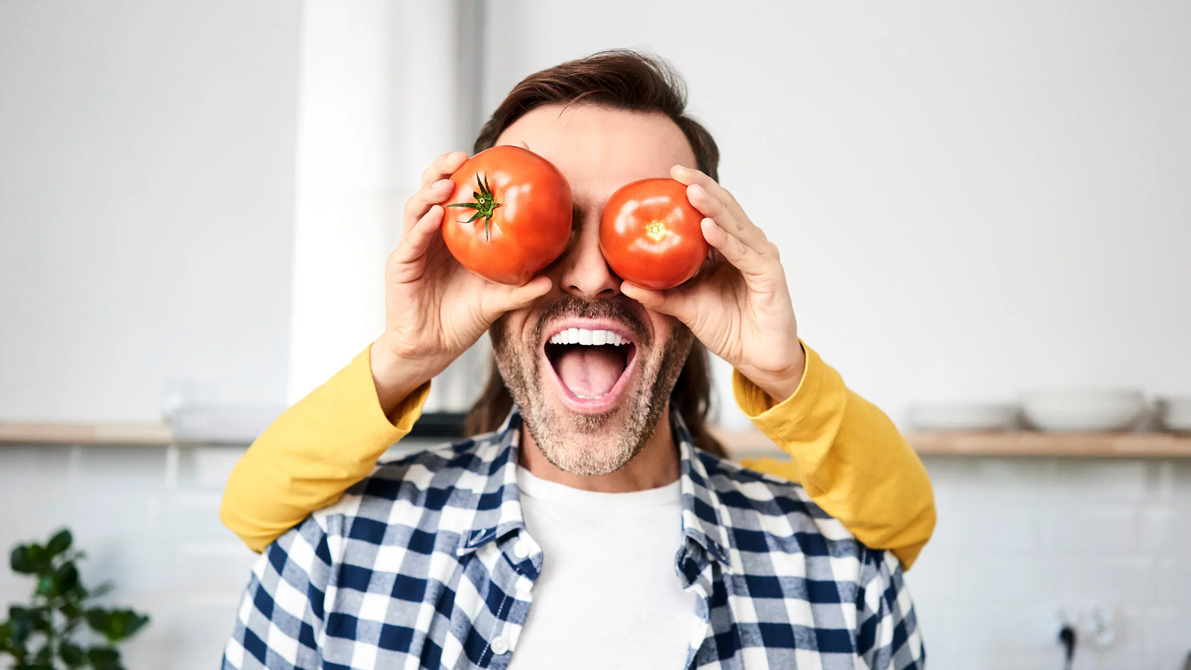 Mies suu auki iloisena, takana oleva lapsi on peittänyt miehen silmät omenalla ja tomaatilla.