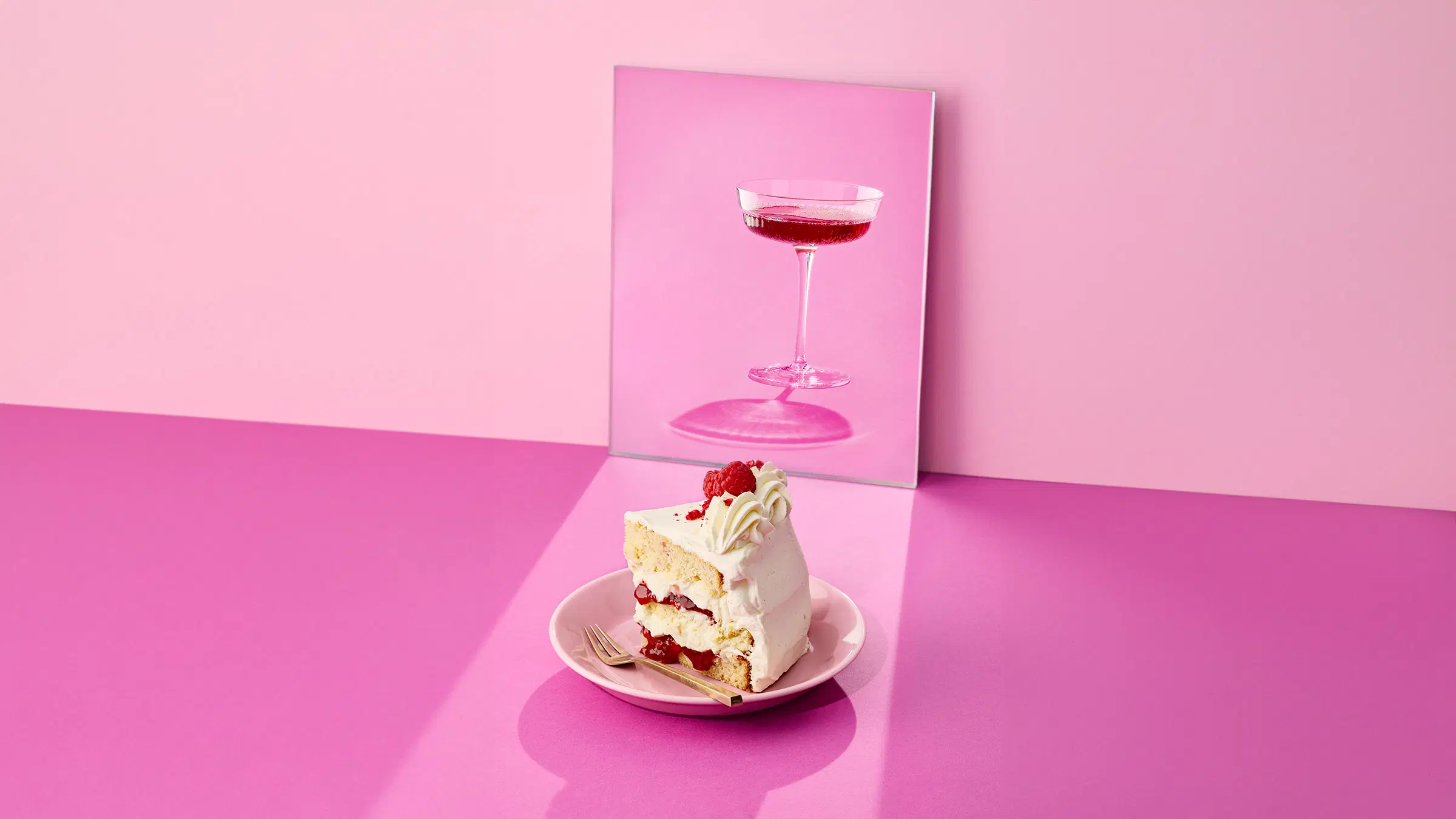 Lautasella pala vadelma-valkosuklaakakkua ja taustalla peilissä näkyy lasillinen juomaa