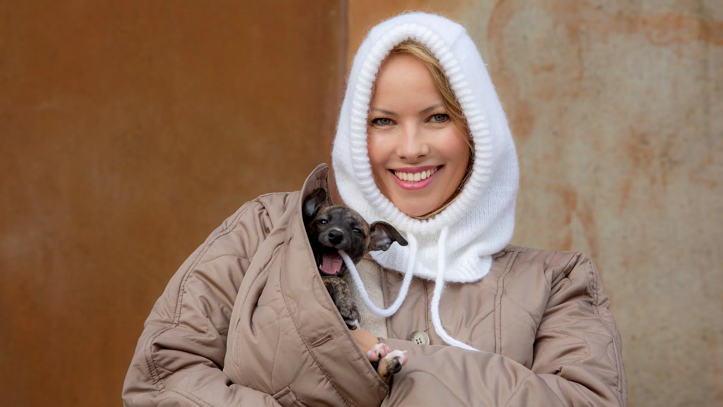 Nainen, joka on pukeutunut balaclavaan ja jonka sylissä on pieni koira.