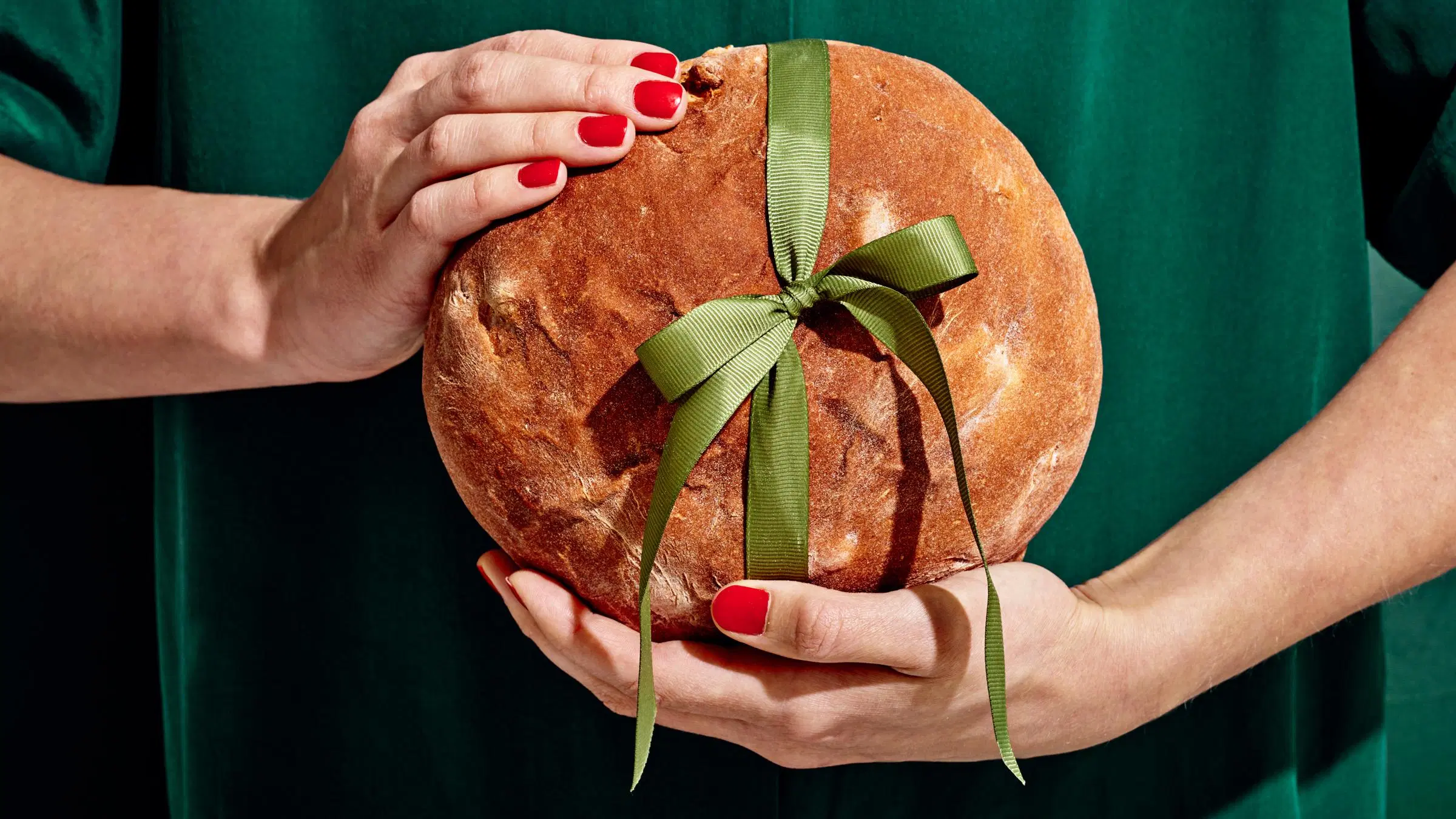 Kädet pitävät rusetilla koristeltua joululeipää.