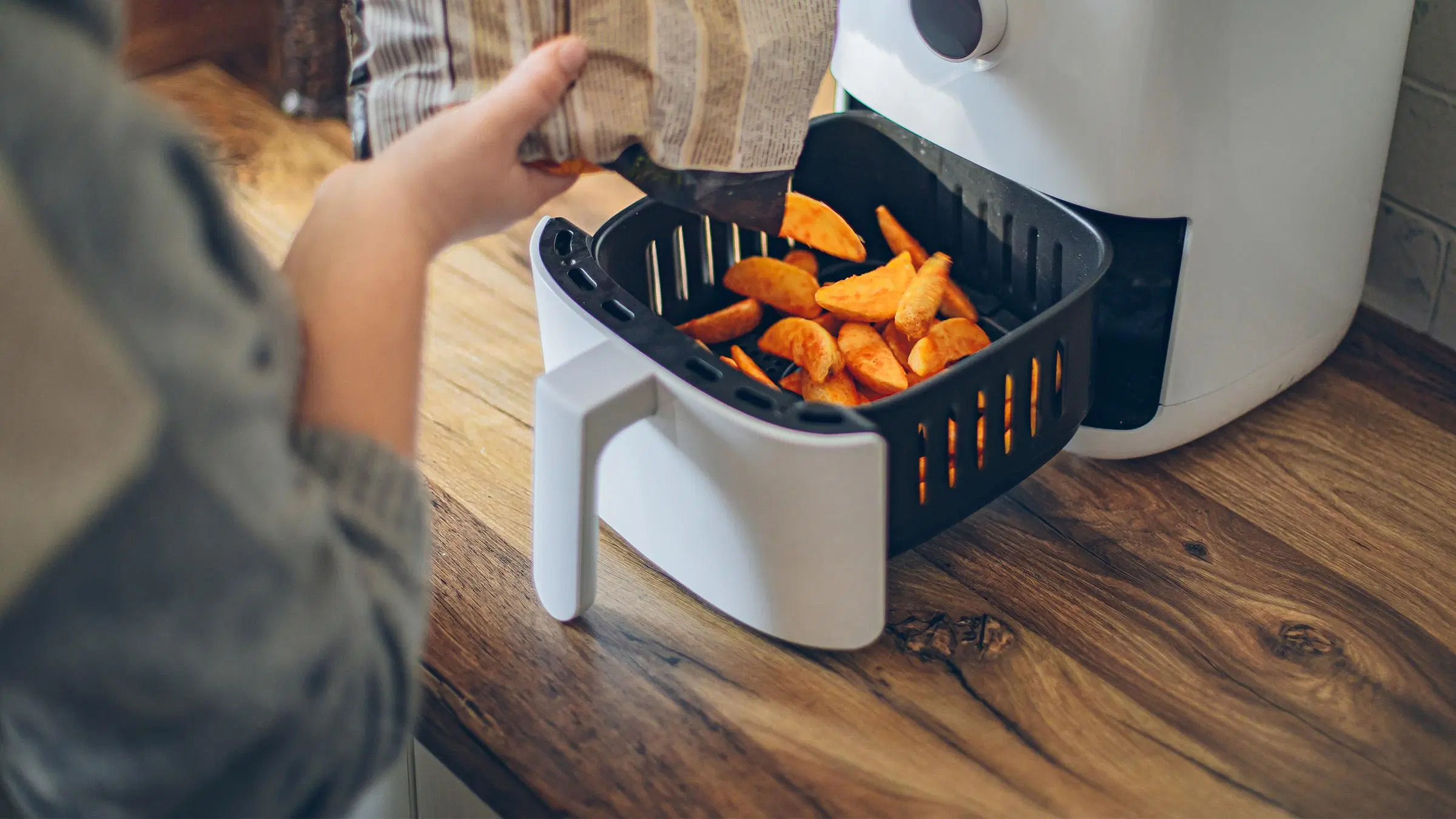 Ihminen kaataa lohkoperunoita airfryerin koriin. 