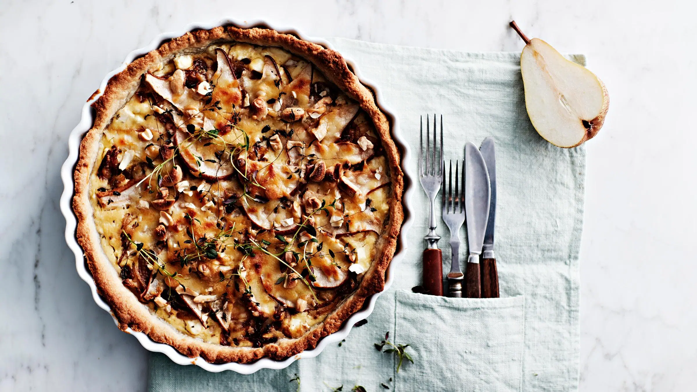 Kokonainen feta-päärynäpiirakka sekä haarukoita ja veitsiä.