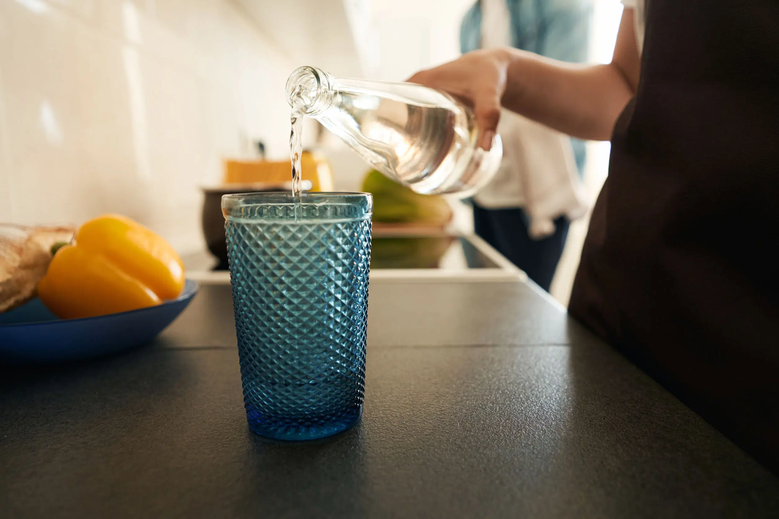 Nainen kaataa lasipullosta vettä lasiin keittiössä.