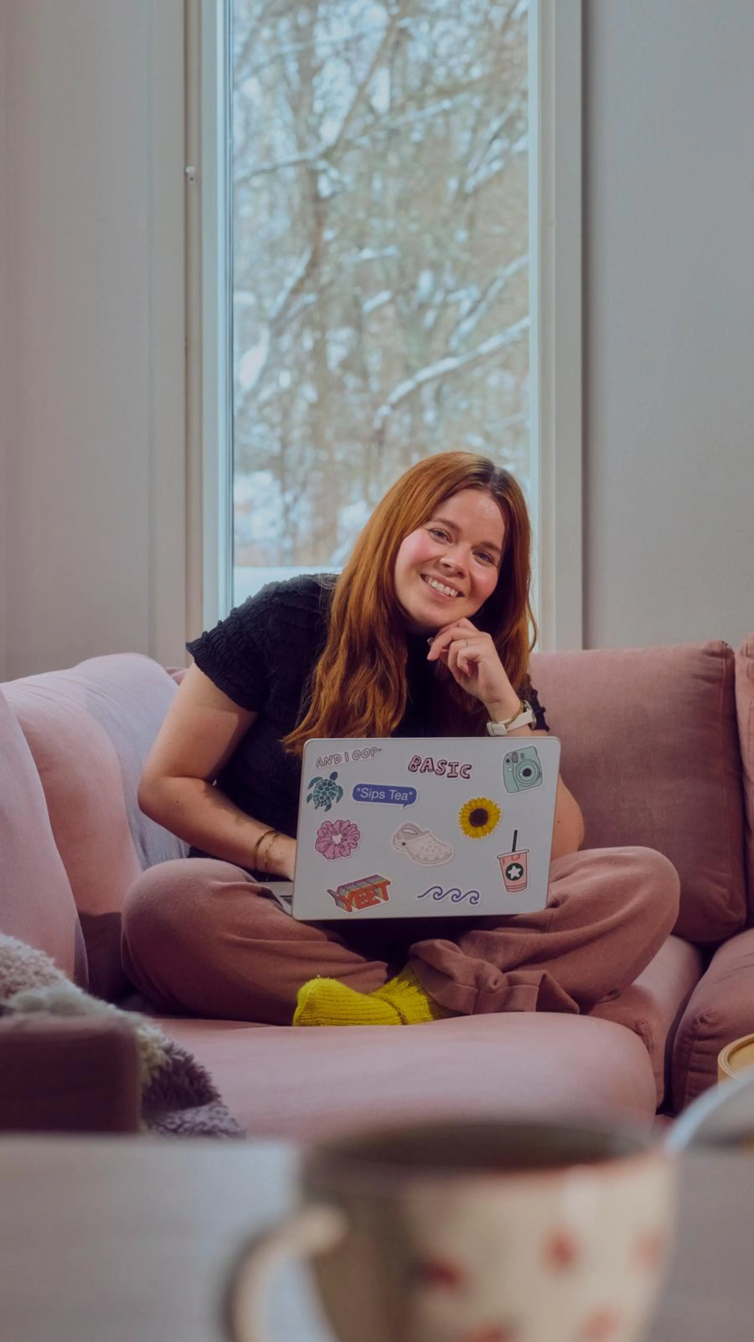 Salla Salmela istuu vaaleanpunaisella sohvalla kannettava tietokone sylissään.