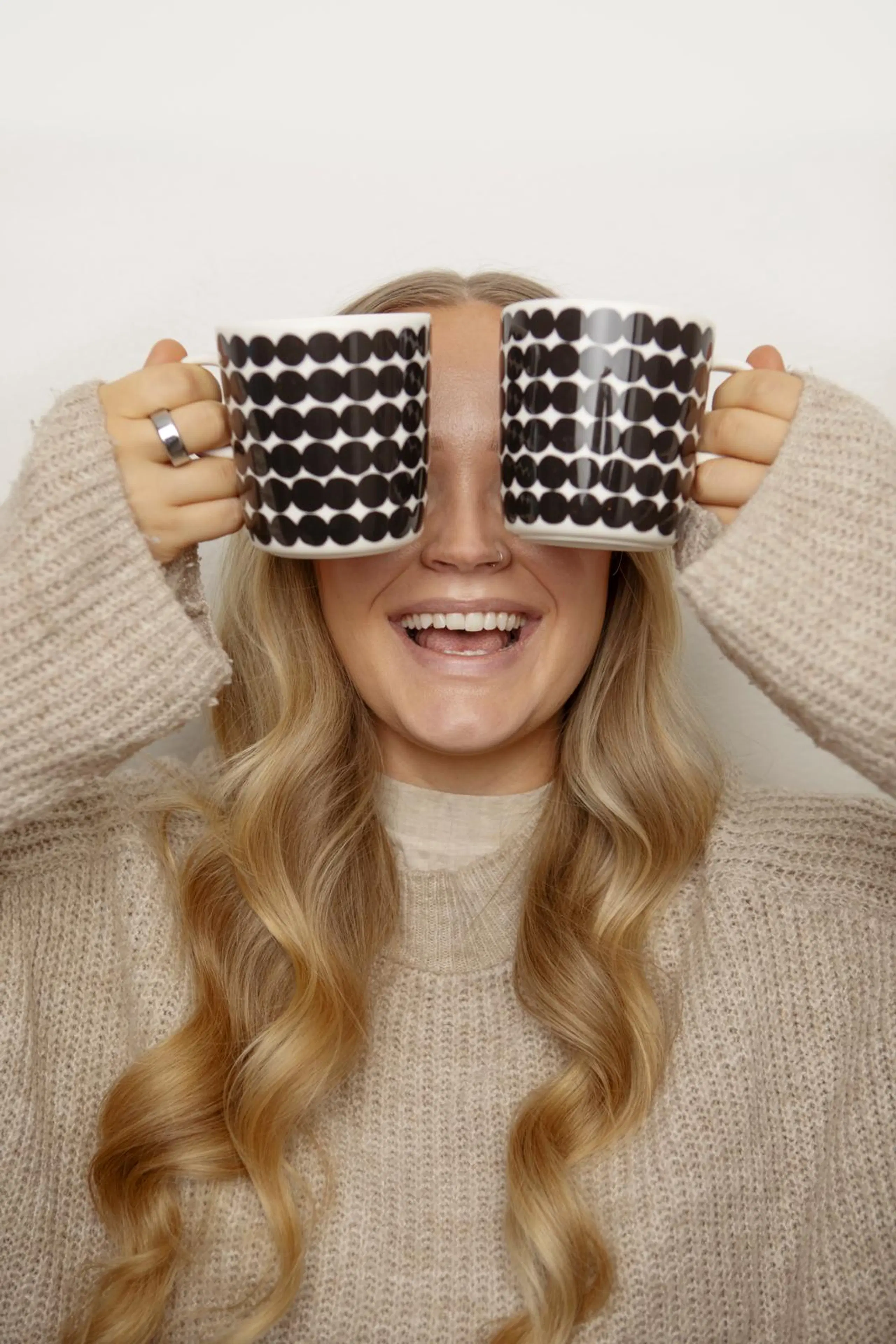 Emilia Tukiainen nauraa ja pitelee silmien edessä kahvikuppeja