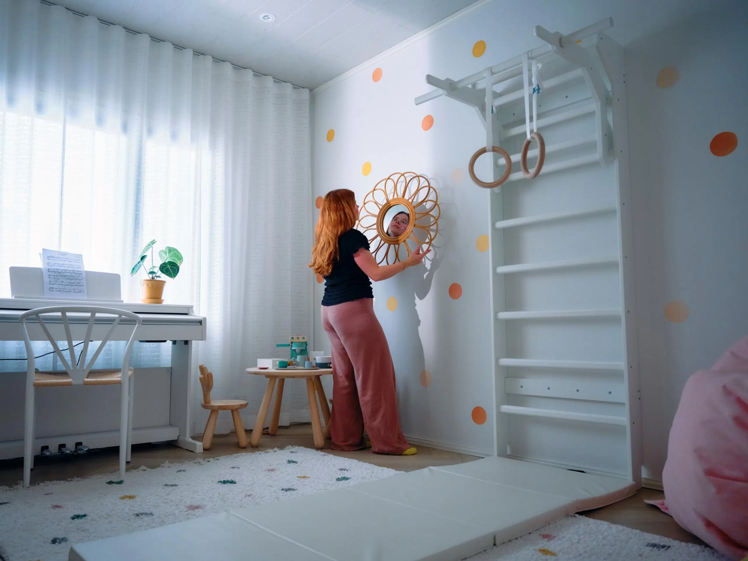 Salla Salmela sovittaa pyöreää peiliä seinälle. Huoneessa on lasten pöytäryhmä, puolapuut ja voimistelurenkaat.
