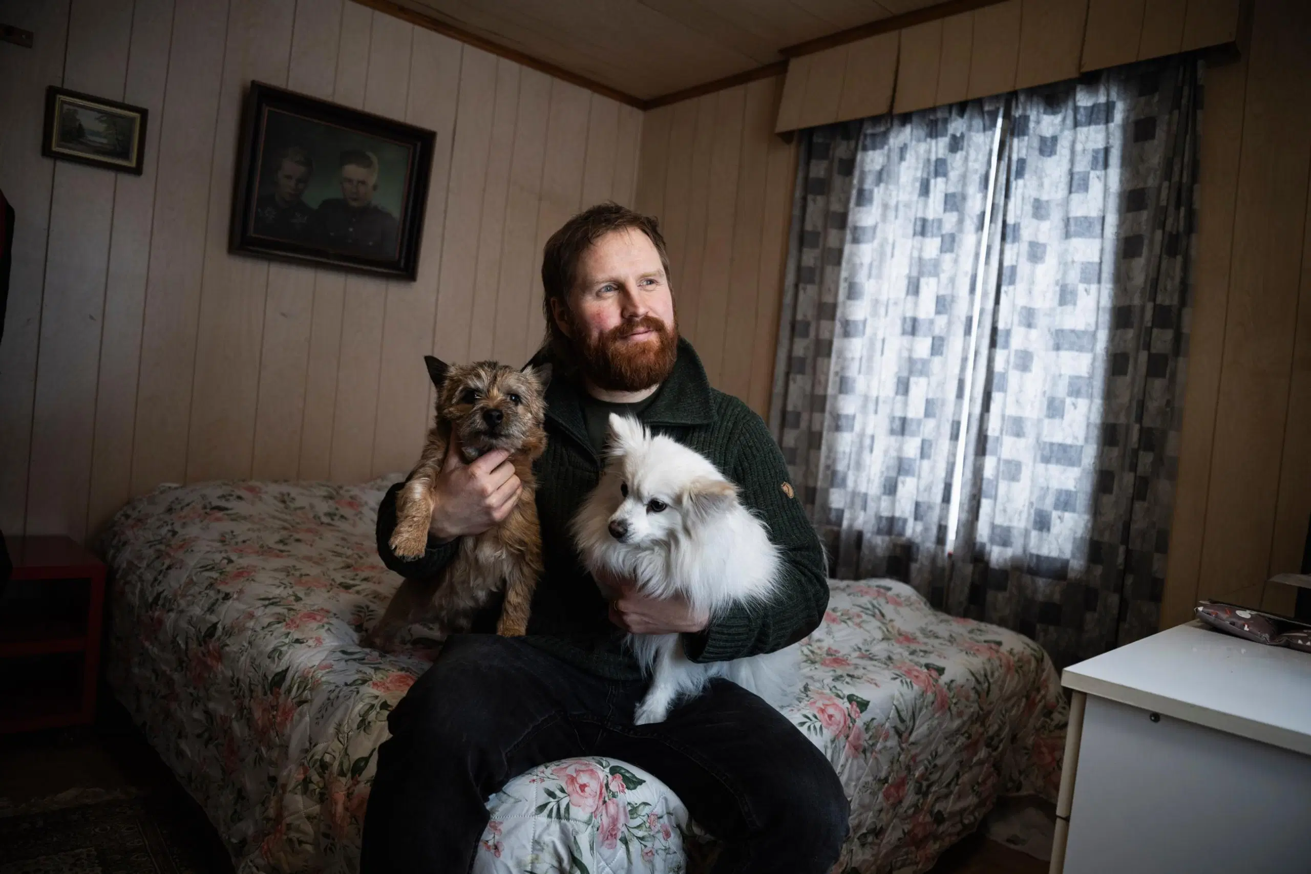 Tommi Manninen istuu sängyllä kaksi koiraa sylissään.