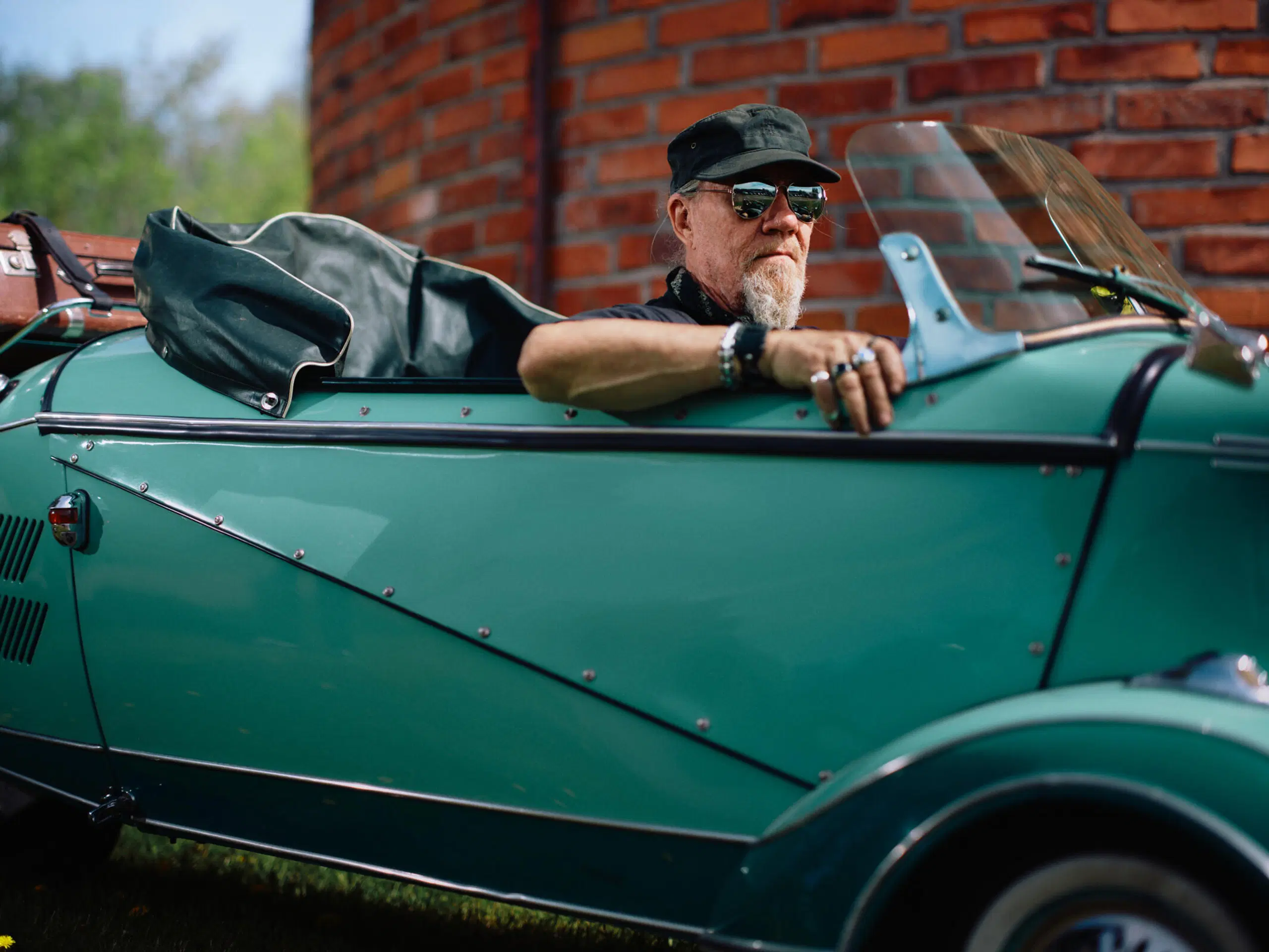 Seppo Sjögren aurinkolasit ja hattu päässään autonsa ratissa.