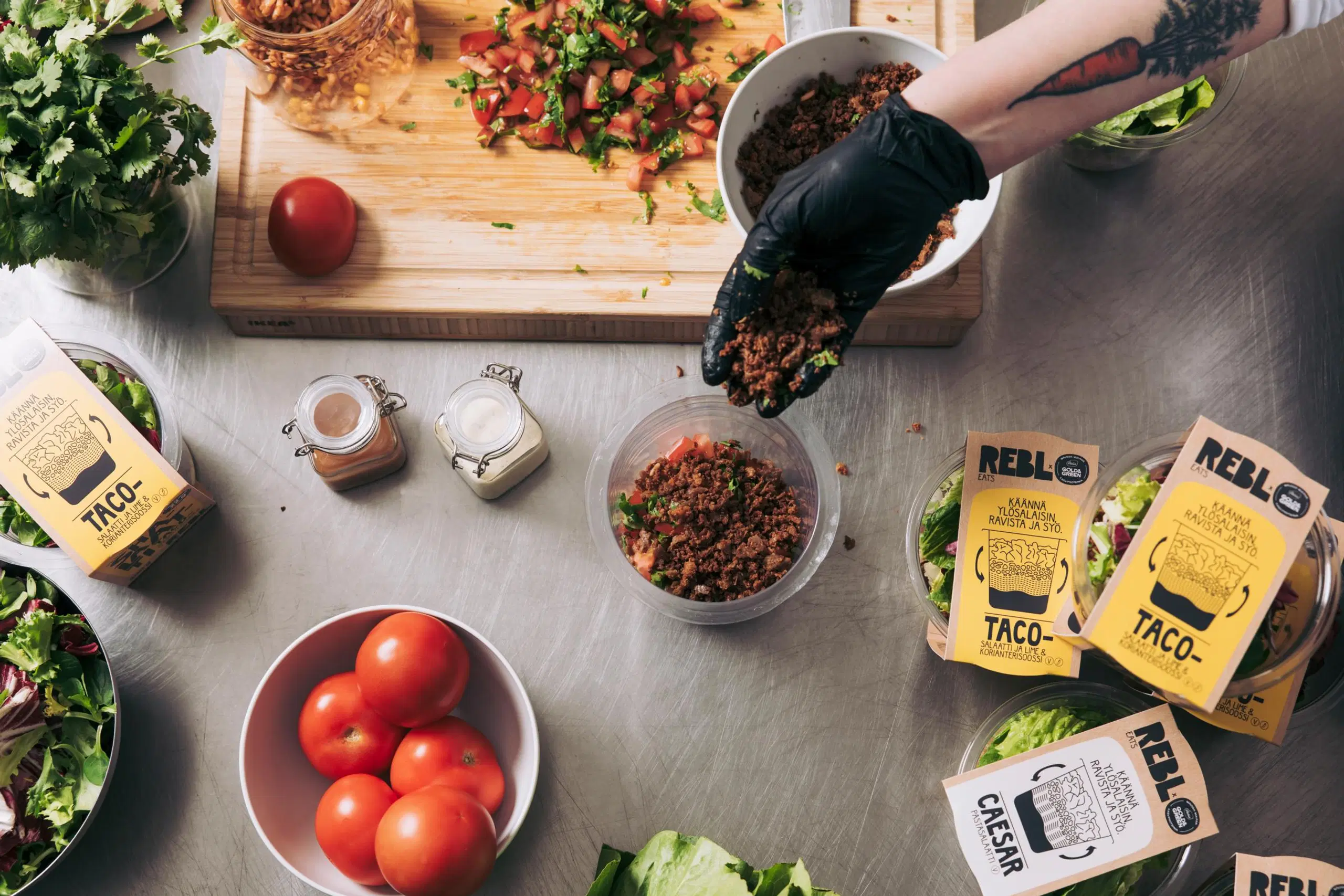 Käsi lisää kasviproteiinia salaattikippoon. Ympärillä muita salaatin raaka-aineita ja tuotepakkauksia.