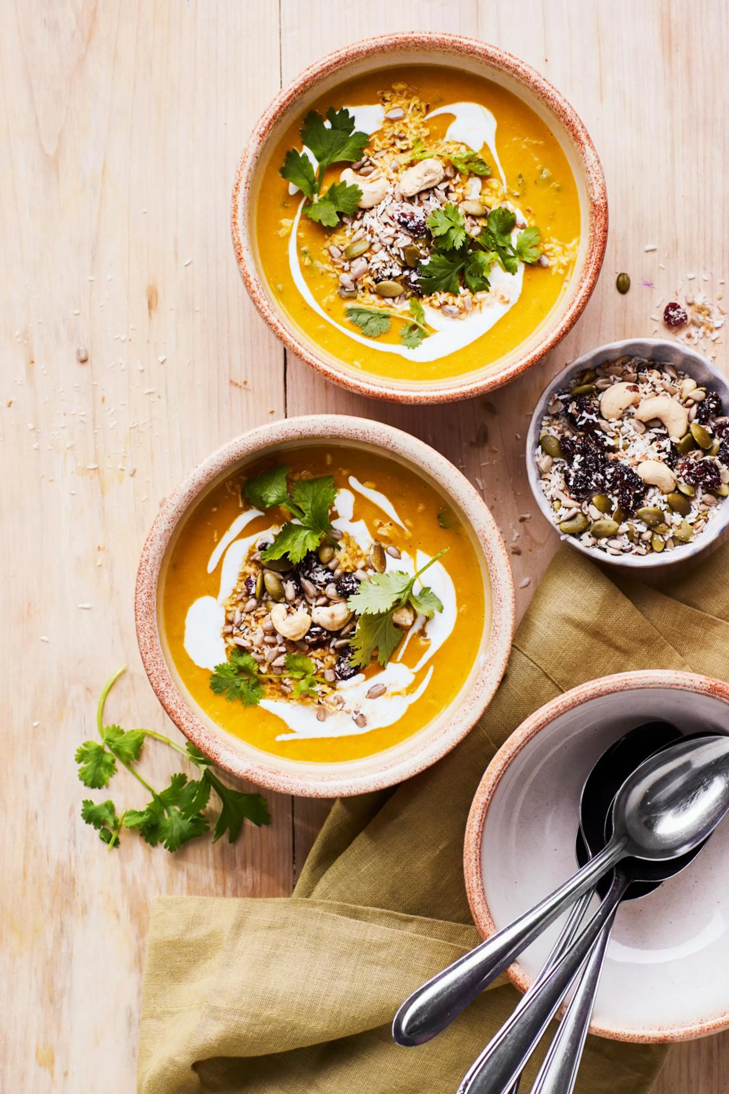 Kaksi lautasellista porkkana-kookoskeittoa. Annosten päällä siemensekoitusta ja korianteria.