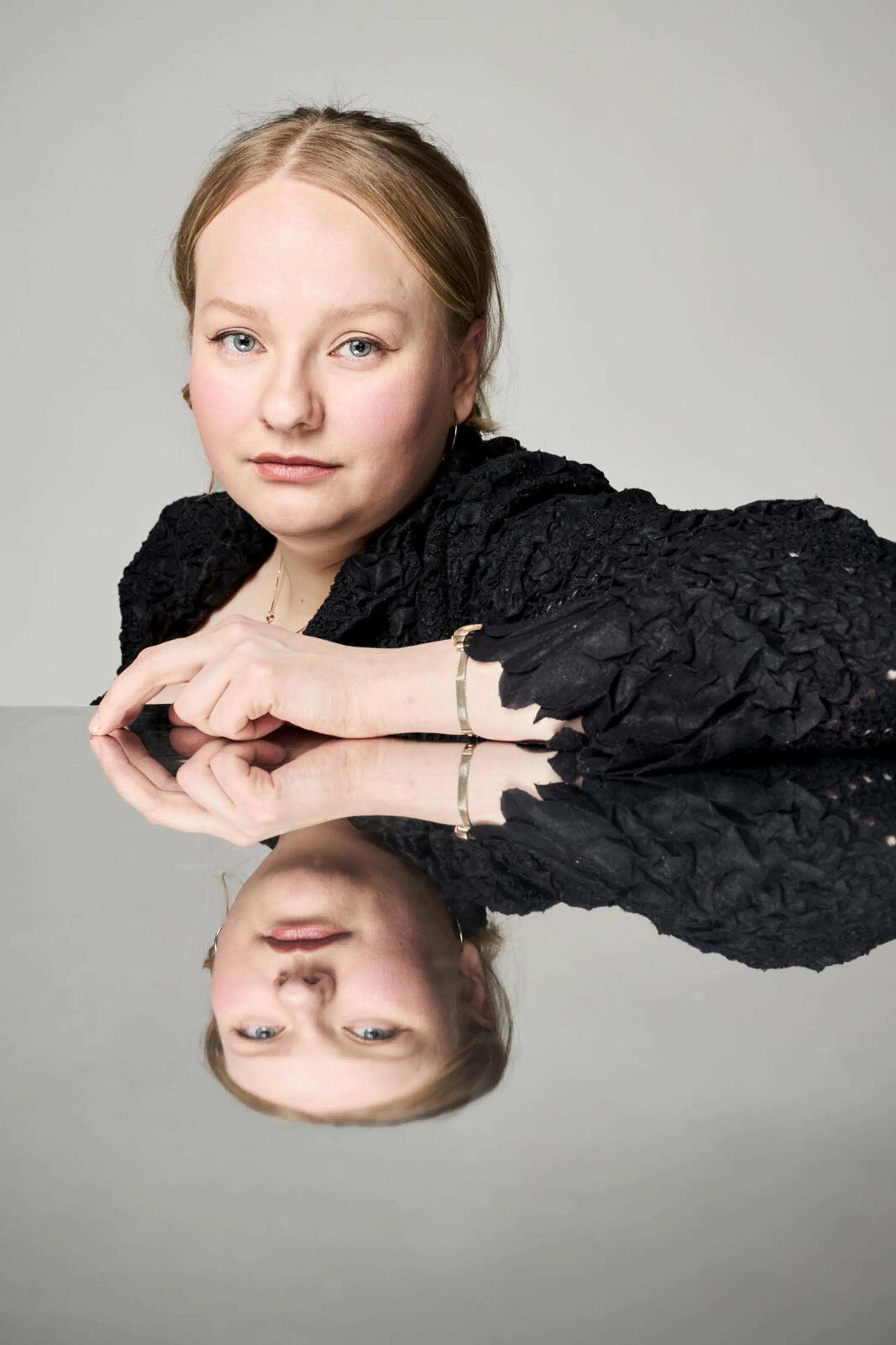 Mielinauhan suunnittelija Enni Lähderinne istuu ja nojaa pöytään, jonka peilipinnasta hän heijastuu.