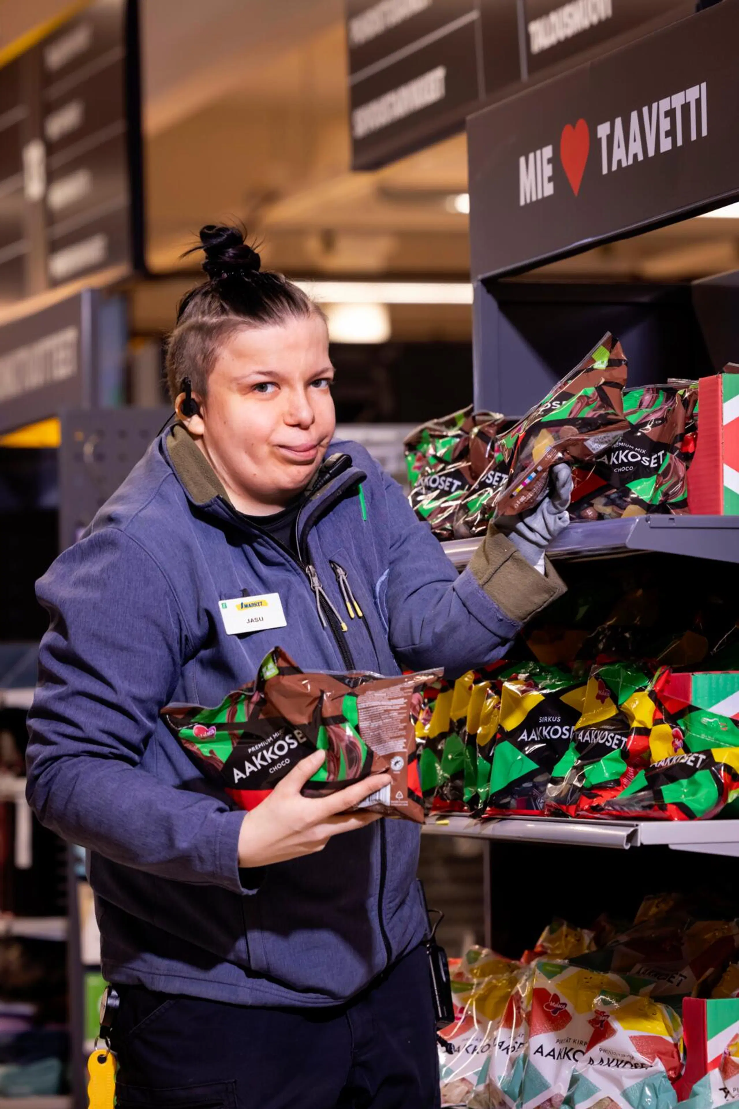 S-marketin myyjä Jasmin Pyykkö seisoo kaupassa karkkihyllyn edessä ja katsoo kameraan.
