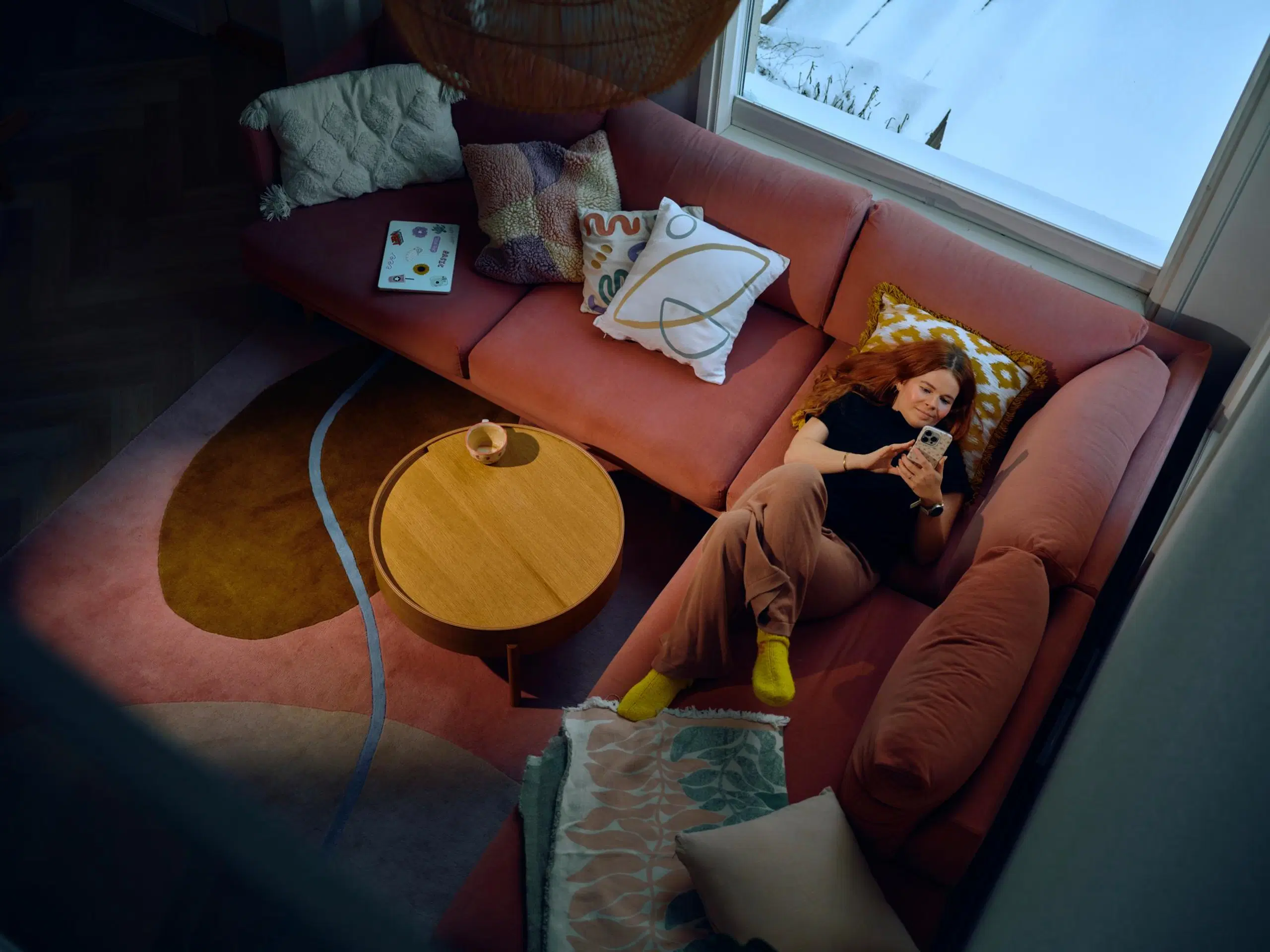 Salla Salmela makaa vaaleanpunaisella sohvalla ja käyttää puhelinta.