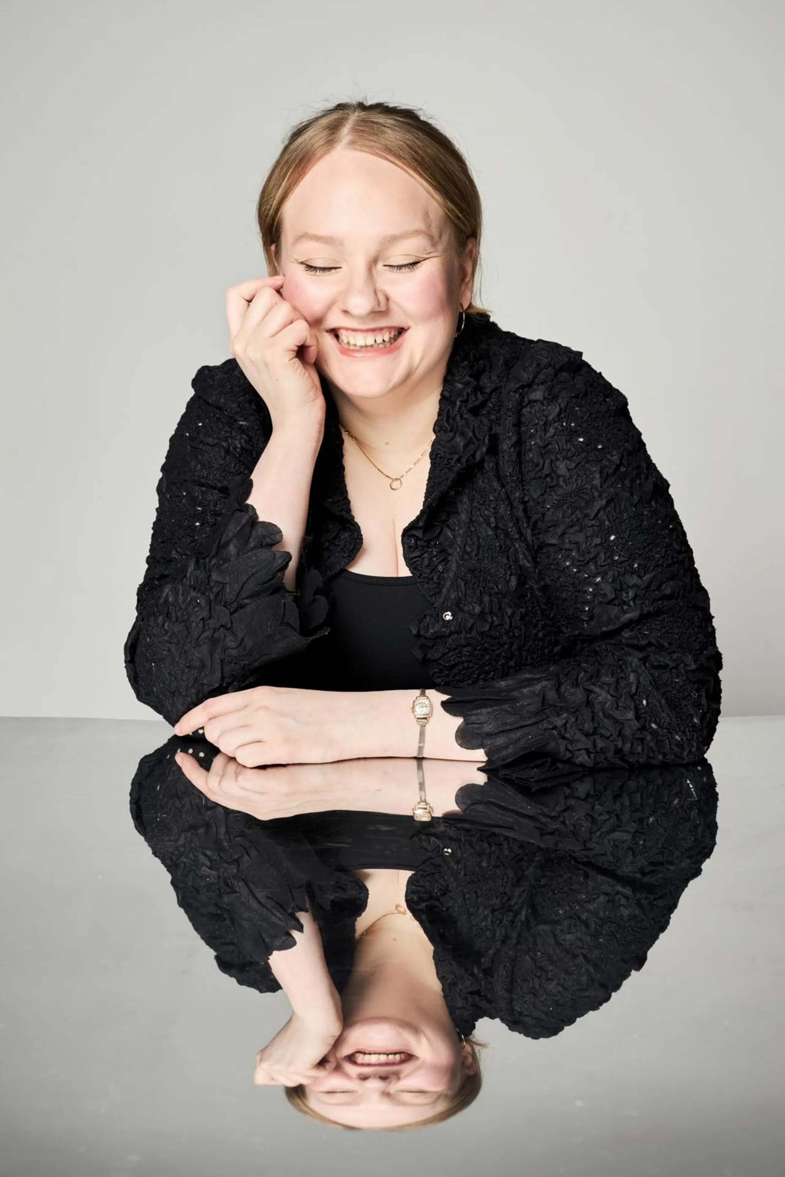 Enni Lähderinne nojaa käeensä ja nauraa silmät suljettuna.