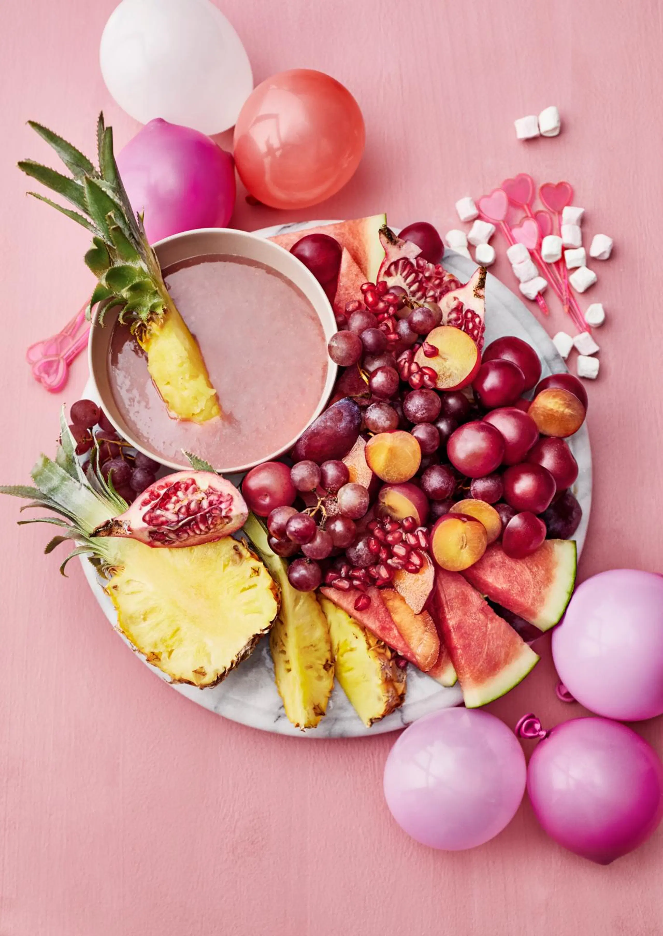 Puolukka-valkosuklaadippi ja hedelmiä vaaleanpunaisella taustalla