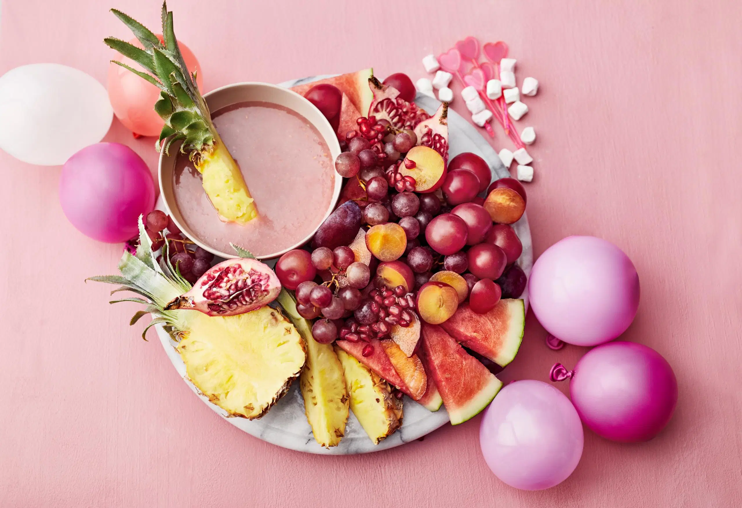 Puolukka-valkosuklaadippi ja hedelmiä vaalenpunaisella taustalla