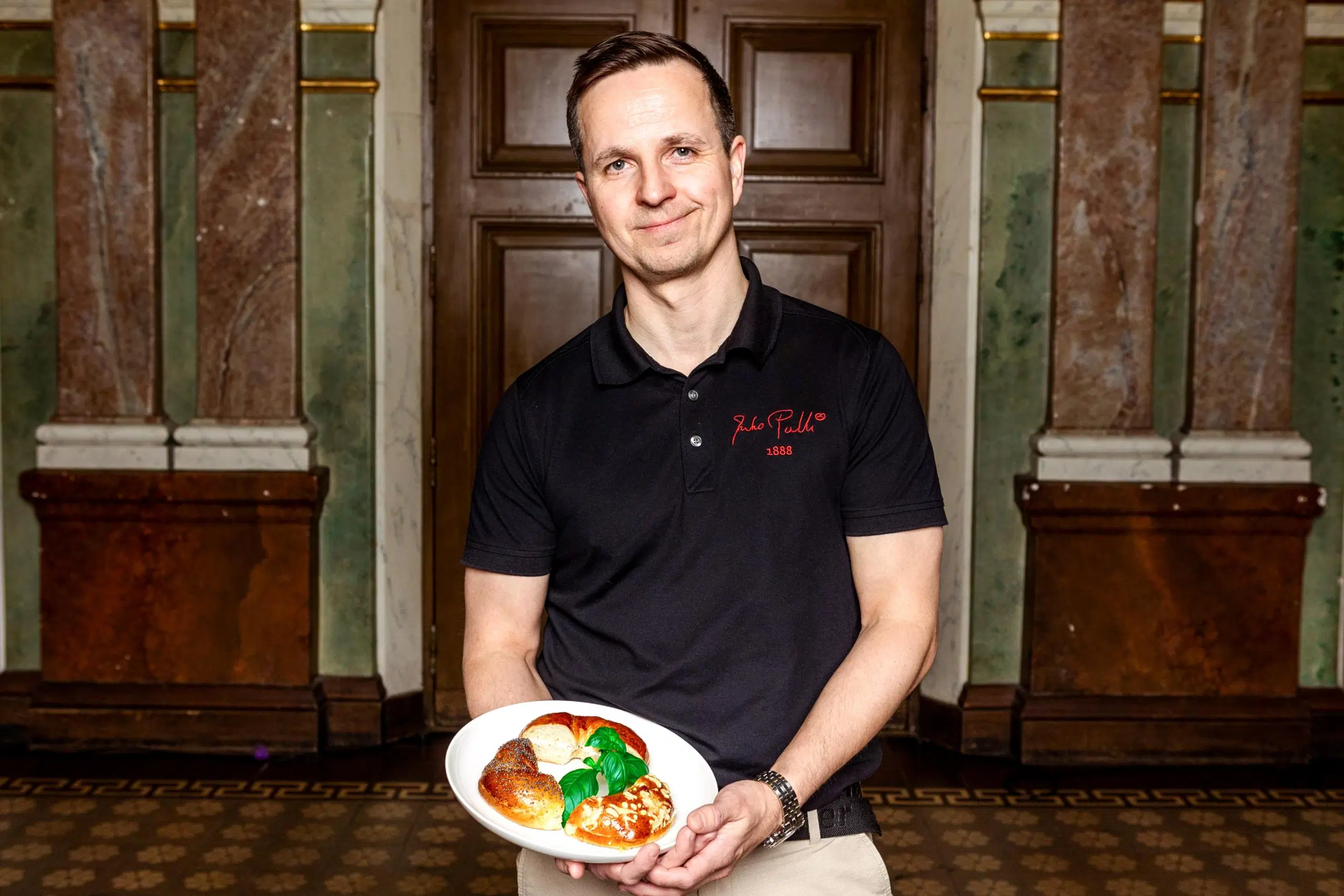 Antti Helkala käsissään lautanen, jolla on kolme palaa bagel-tyylistä leipää