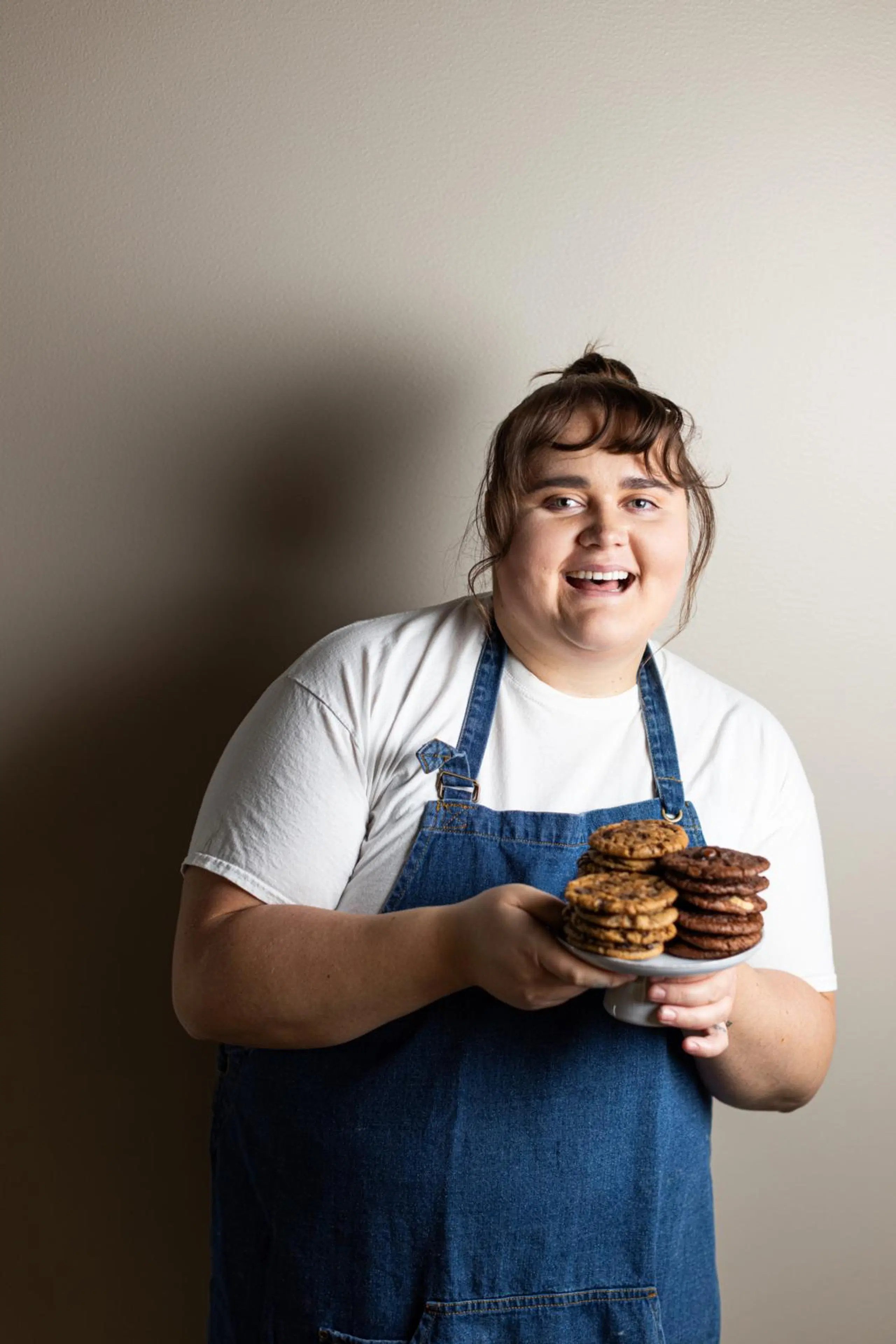 Hymyilevä Erika Poussa käsissään pieni tarjotin, jolla on kolme keksipinoa