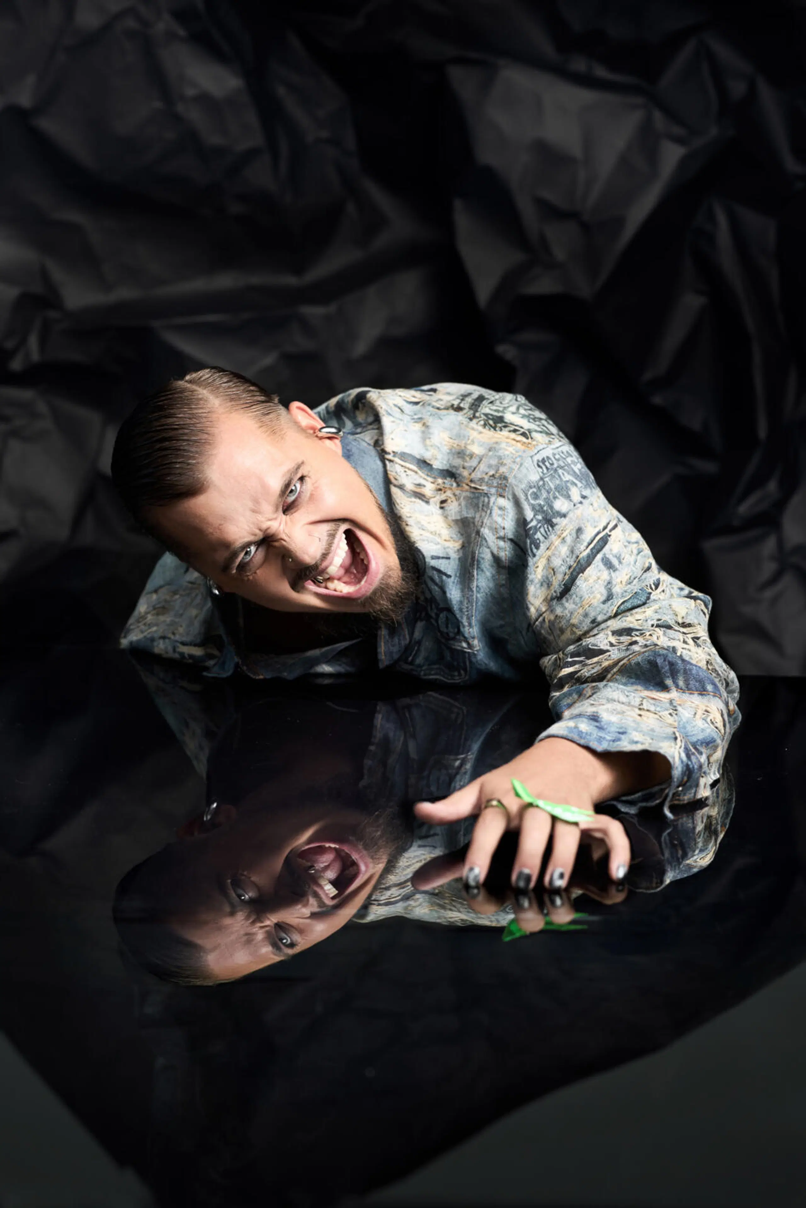 Jere Pöyhönen seisoo mustan rypystetyn taustakankaan edessä farkkuasussa ja ilmeilee kameralle.