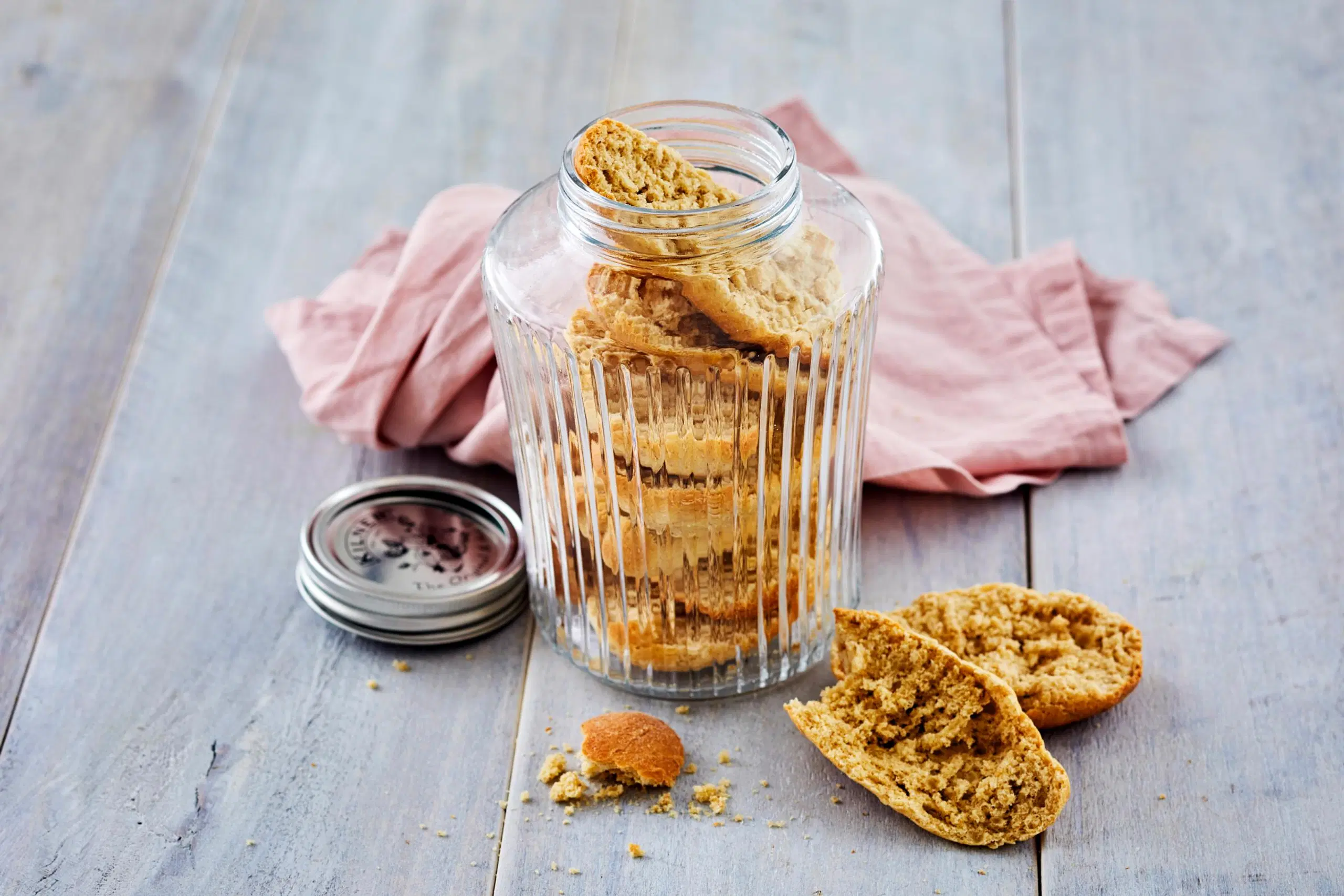 Täysjyväkorppuja lasipurkissa, taustalla vaaleanpunainen keittiöpyyhe