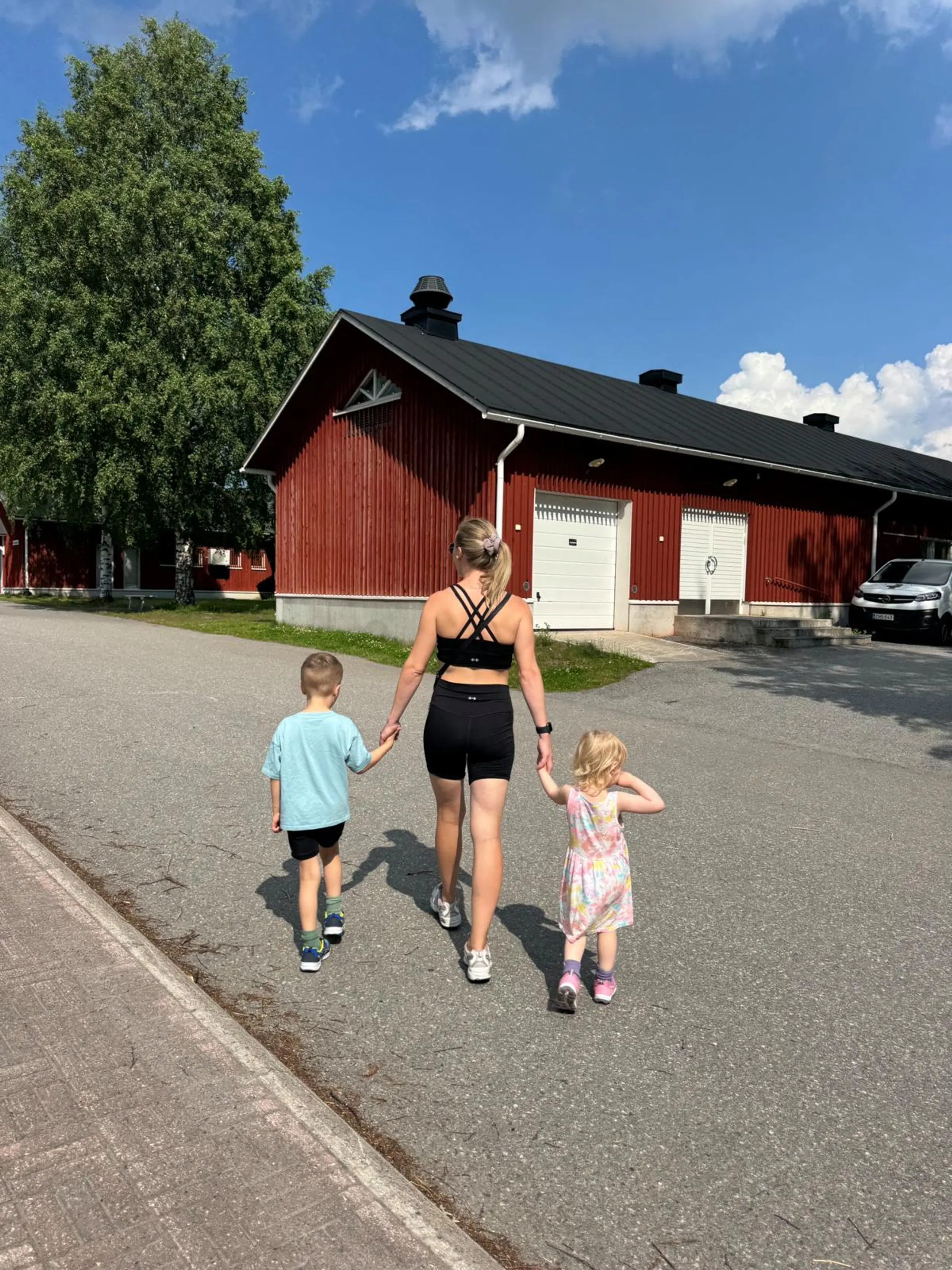 Takaapäin kuvattu Elina Leskinen kävelee käsi kädessä kahden pienen lapsen kanssa