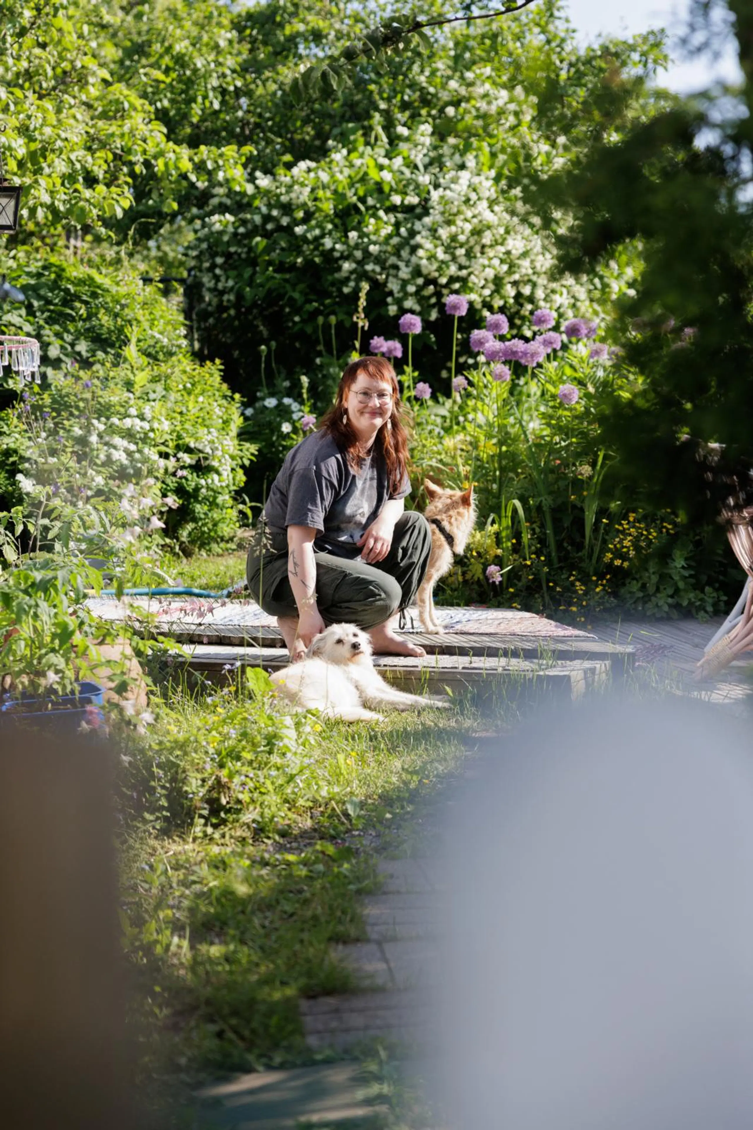 Eeva Naskali istuu puutarhassa ja silittää valkoista koiraa.