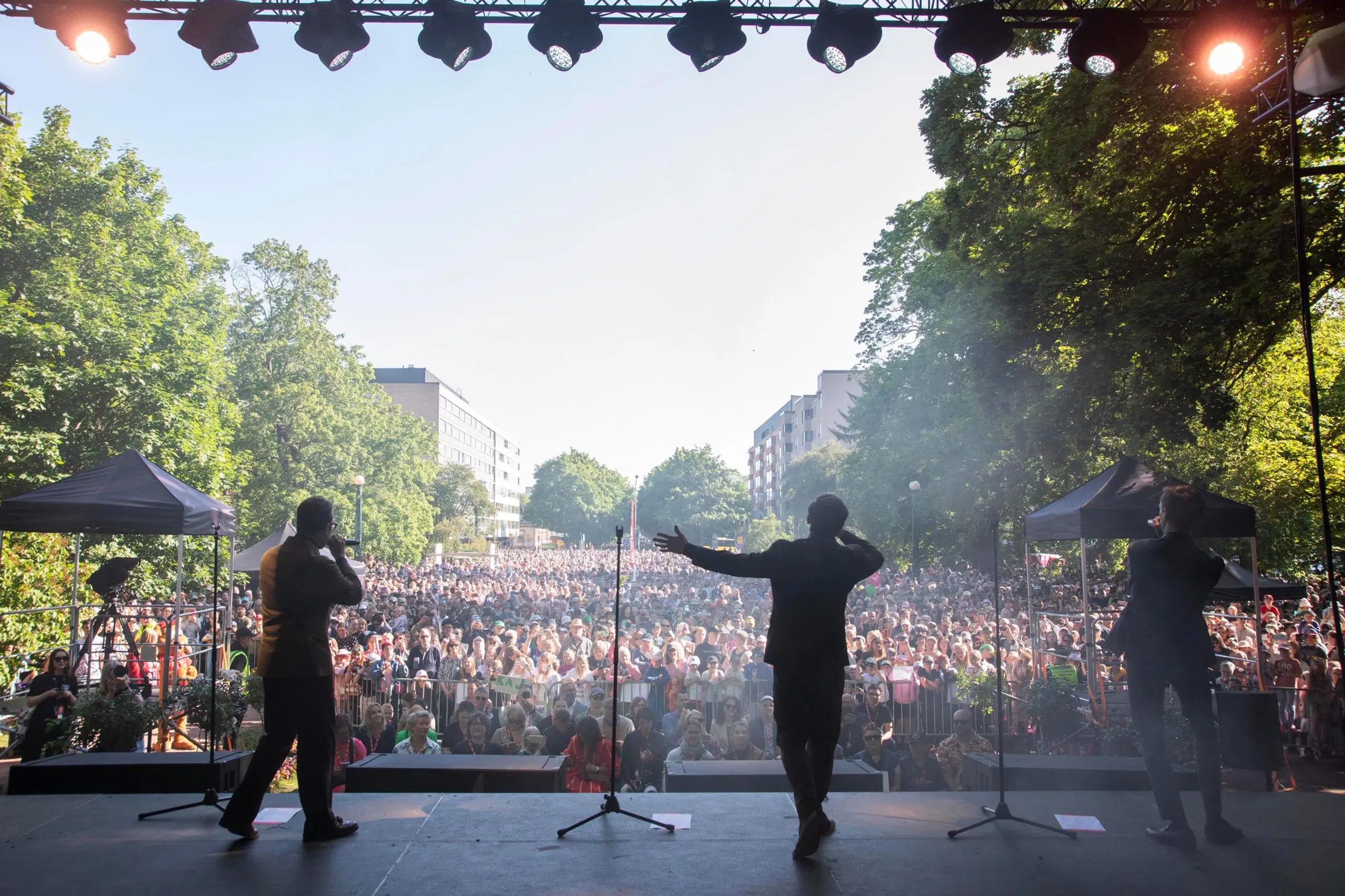 Lavalla oleva KAJ kuvattuna takaapäin ja yleisö kesäisessä puistossa.