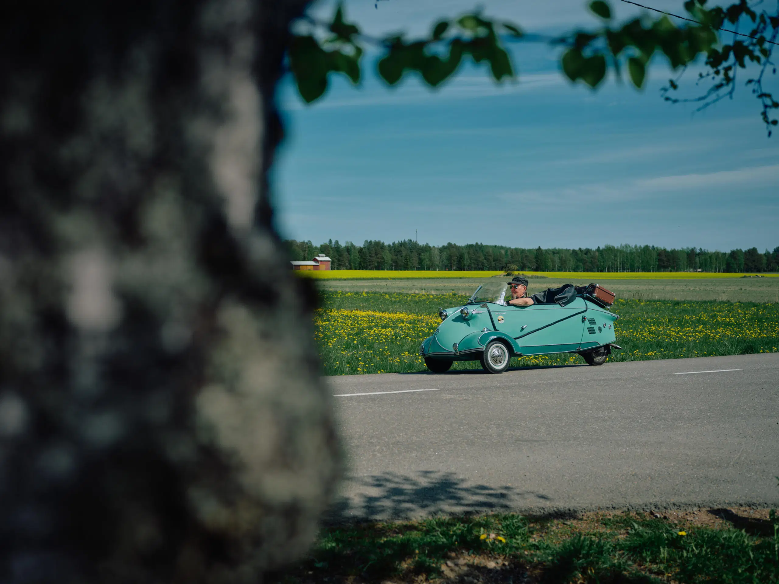Kääpiöauto huristelee pellon reunalla menevällä tiellä.