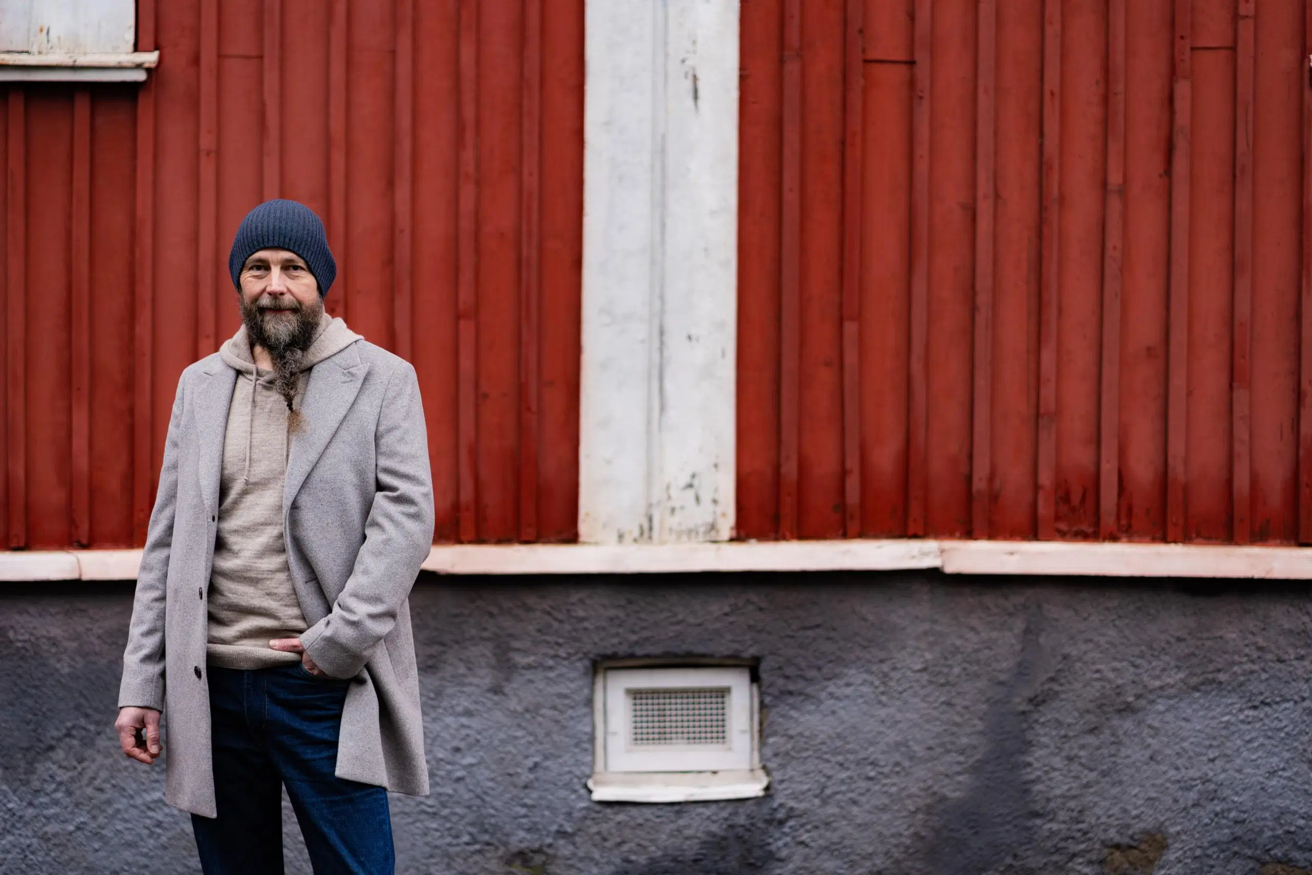 Tero Vesterinen pipossa ja talvitakissa punaisen puutalon edessä