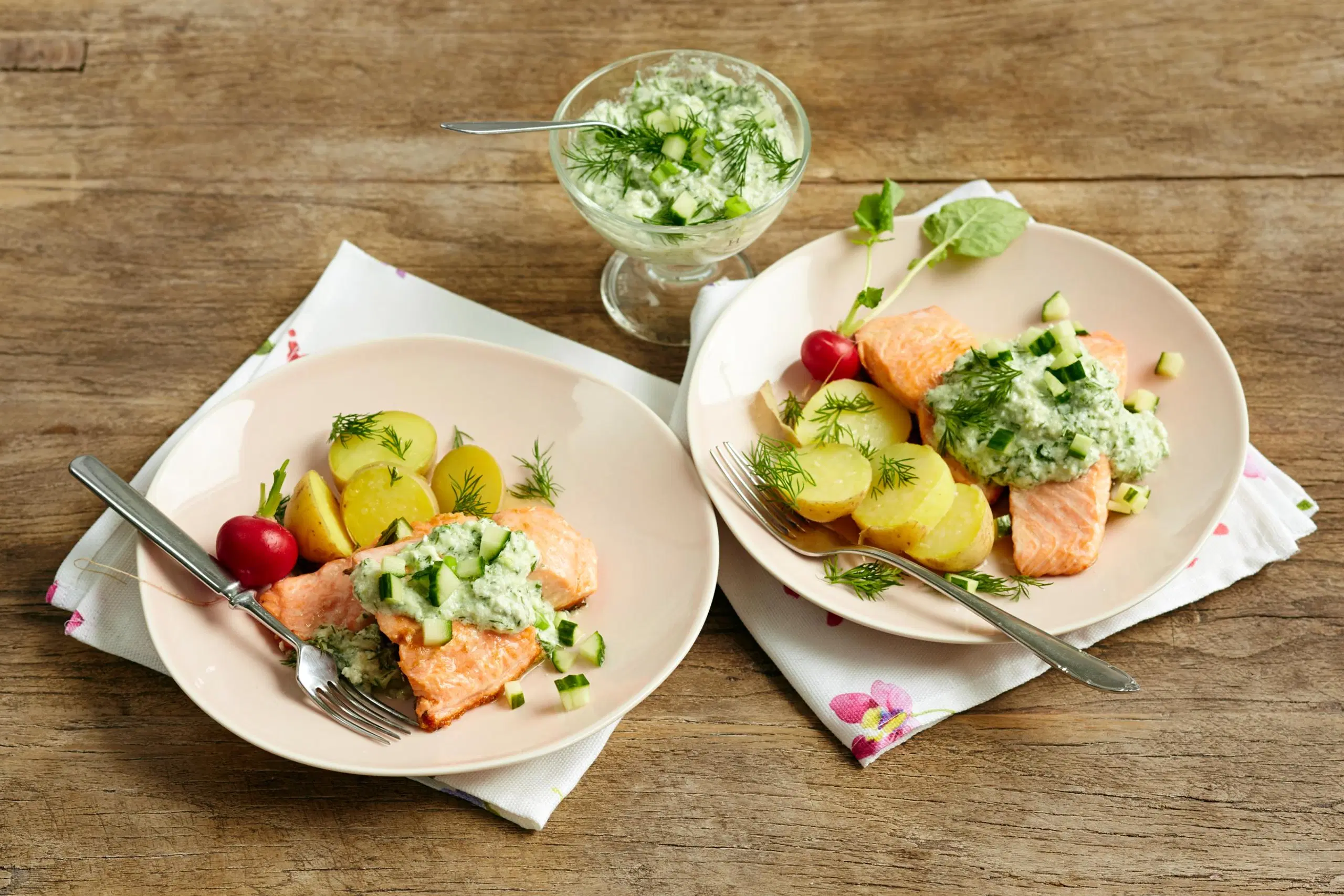 Grillattua lohta, keitettyjä perunoita ja kurkku-fetakastiketta lautasilla.