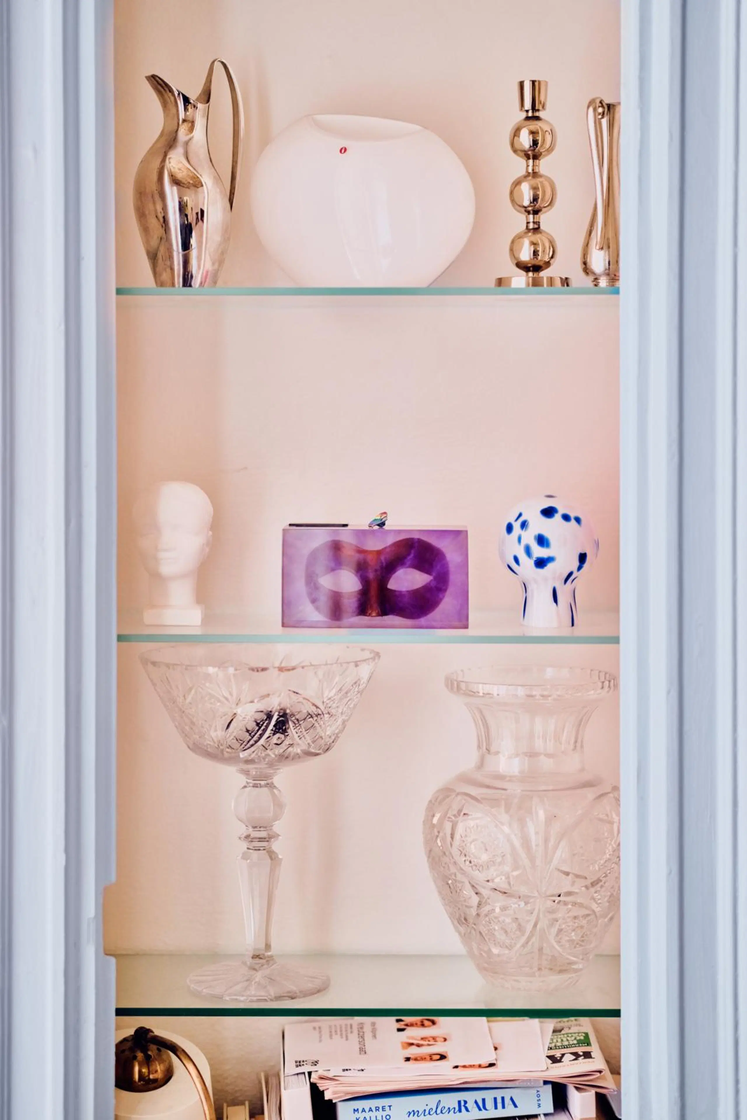 Kapeita lasihyllyjä, joilla on koriste-esineitä, maljakoita, Hymypoika-patsas ja kynttilänjalkoja.