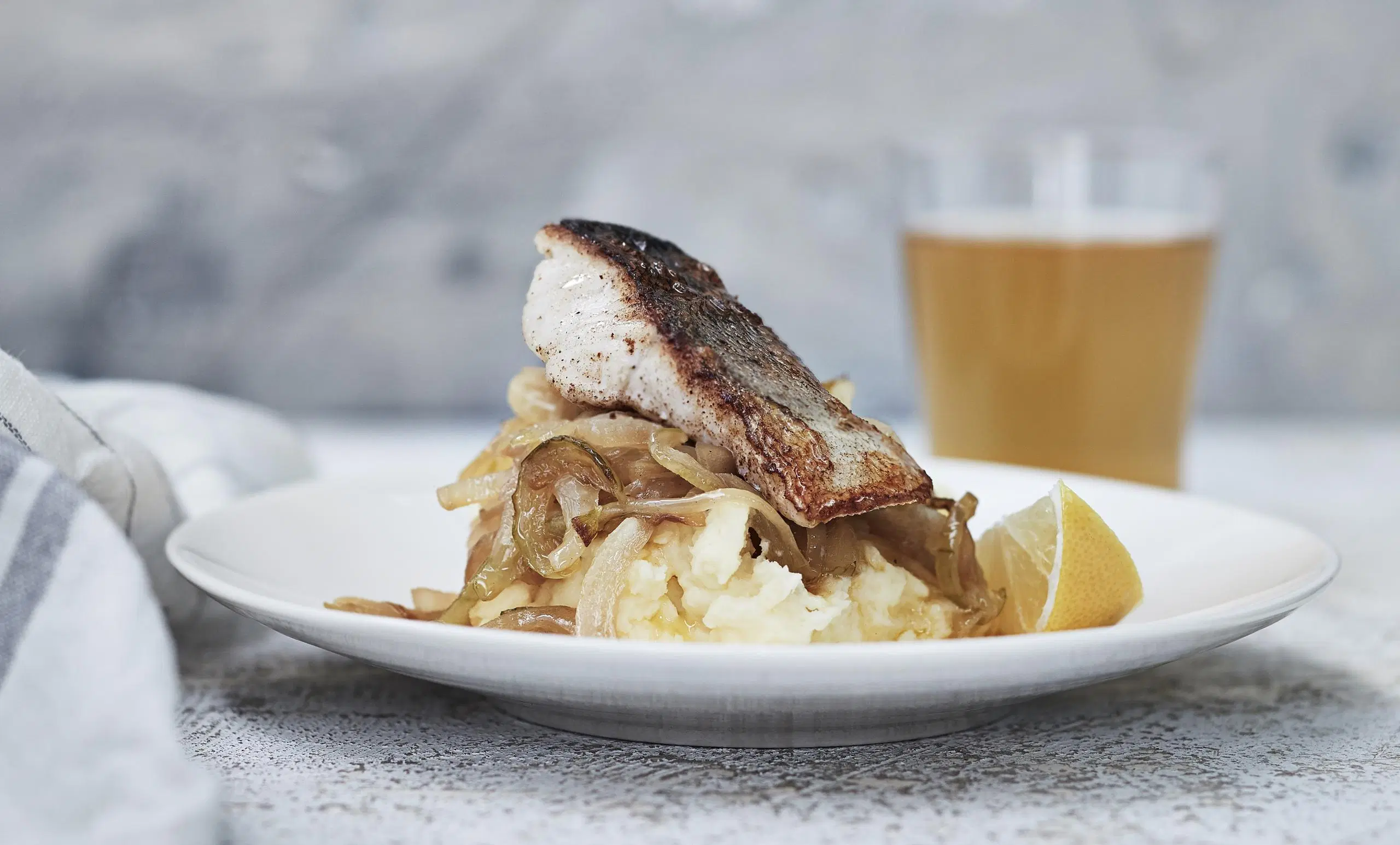 Pannukalaa ja vehnäolutsipulia lautasella, taustalla lasillinen olutta