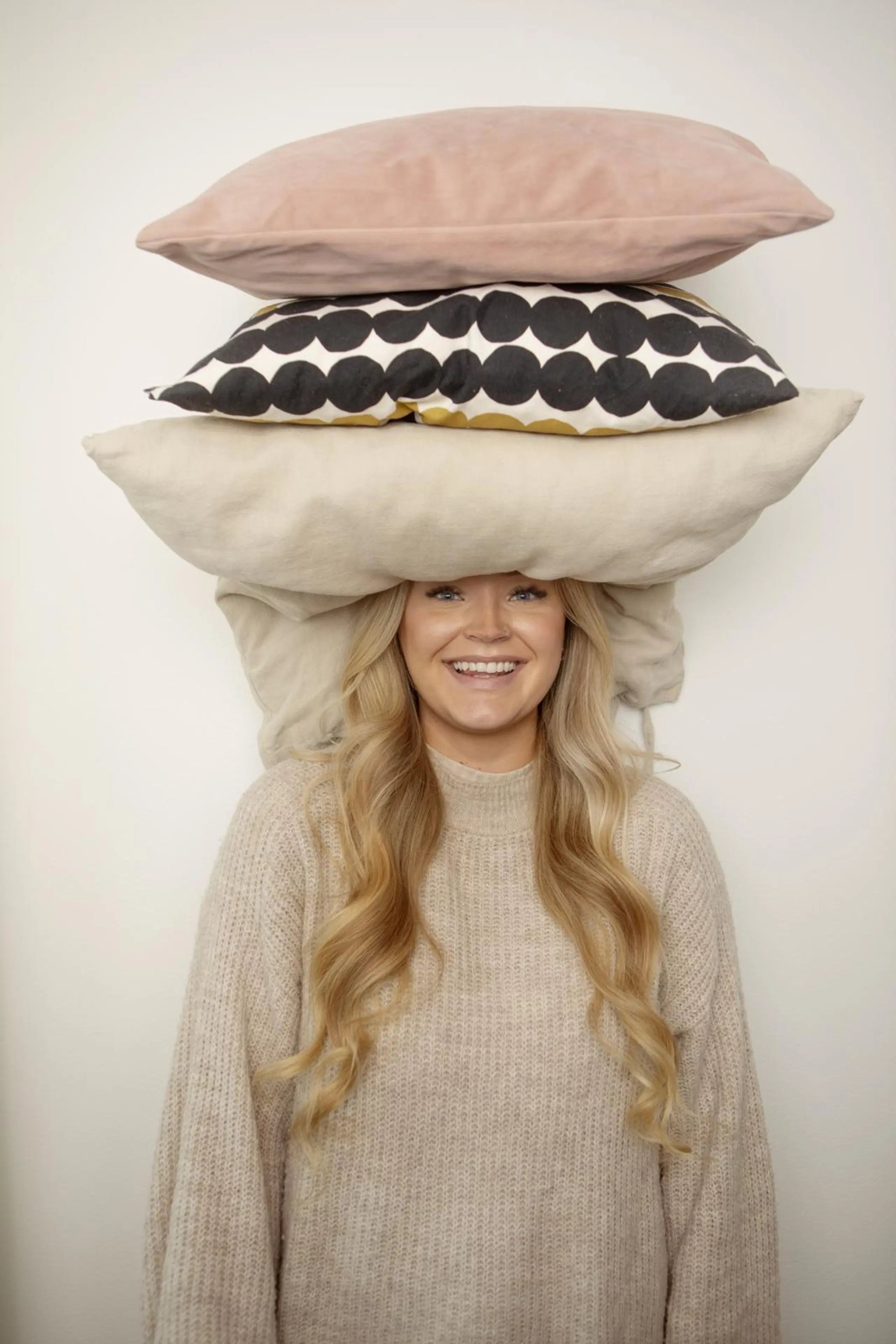 Emilia Tukiainen nauraa kohti kameraa, pään päälle kasattu kolme tyynyä