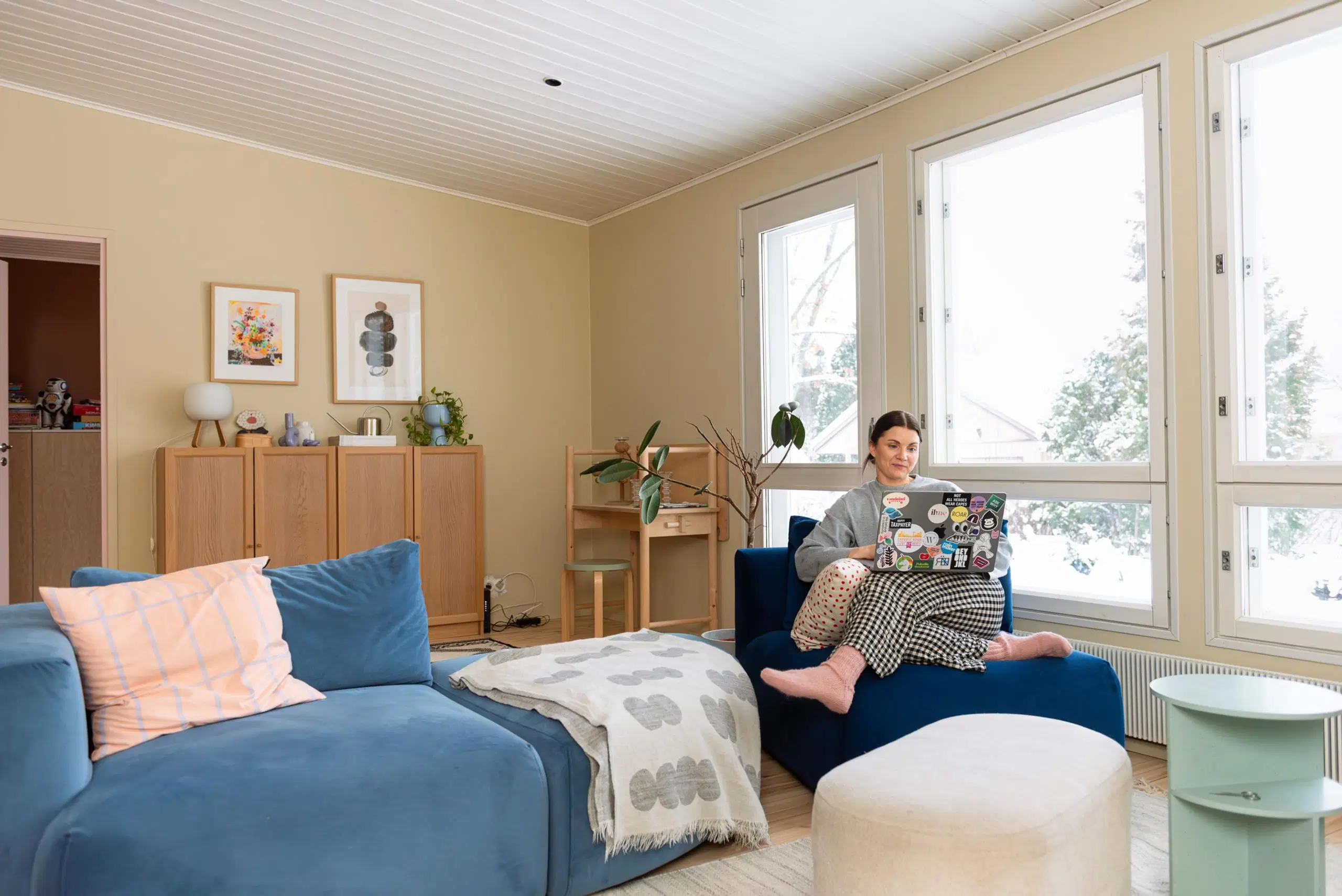 Maru Hautala istuu sohvapalalla ikkunan edessä ja hänellä on sylissään kannettava tietokone.