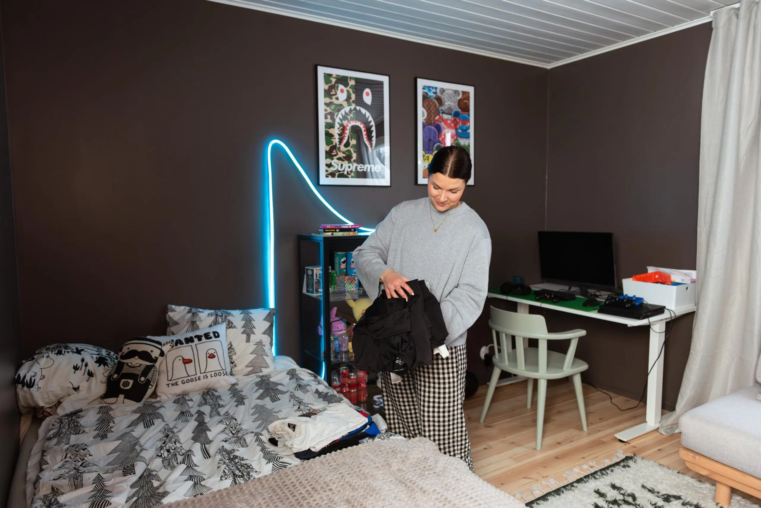 Maru Hautala laittaa vaatepinoa sängylle huoneessa, jossa on tummanharmaat seinät, sänky, valkoinen työpöytä ja musta vitriinikaappi.