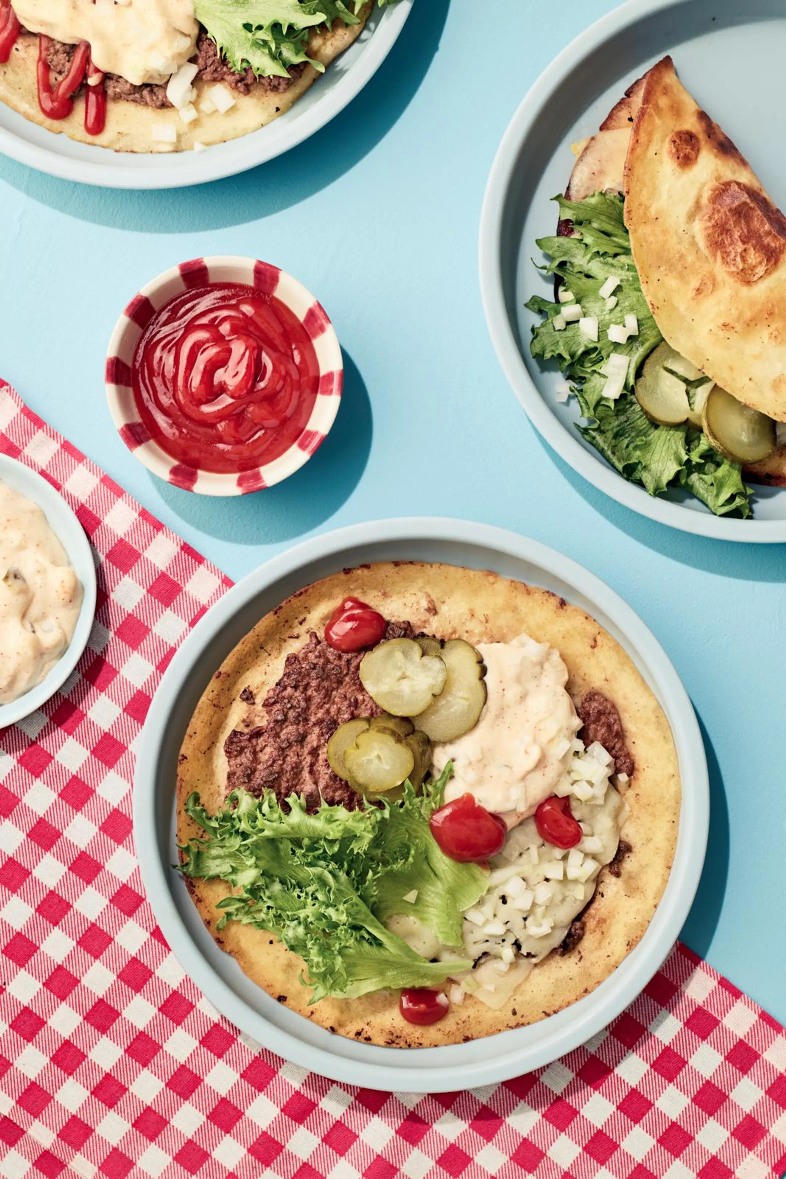 Lautasella burgeritaco, jossa täytteenä jauhelihaa, salaattia, suolakurkkua ja hampurilaiskastiketta.