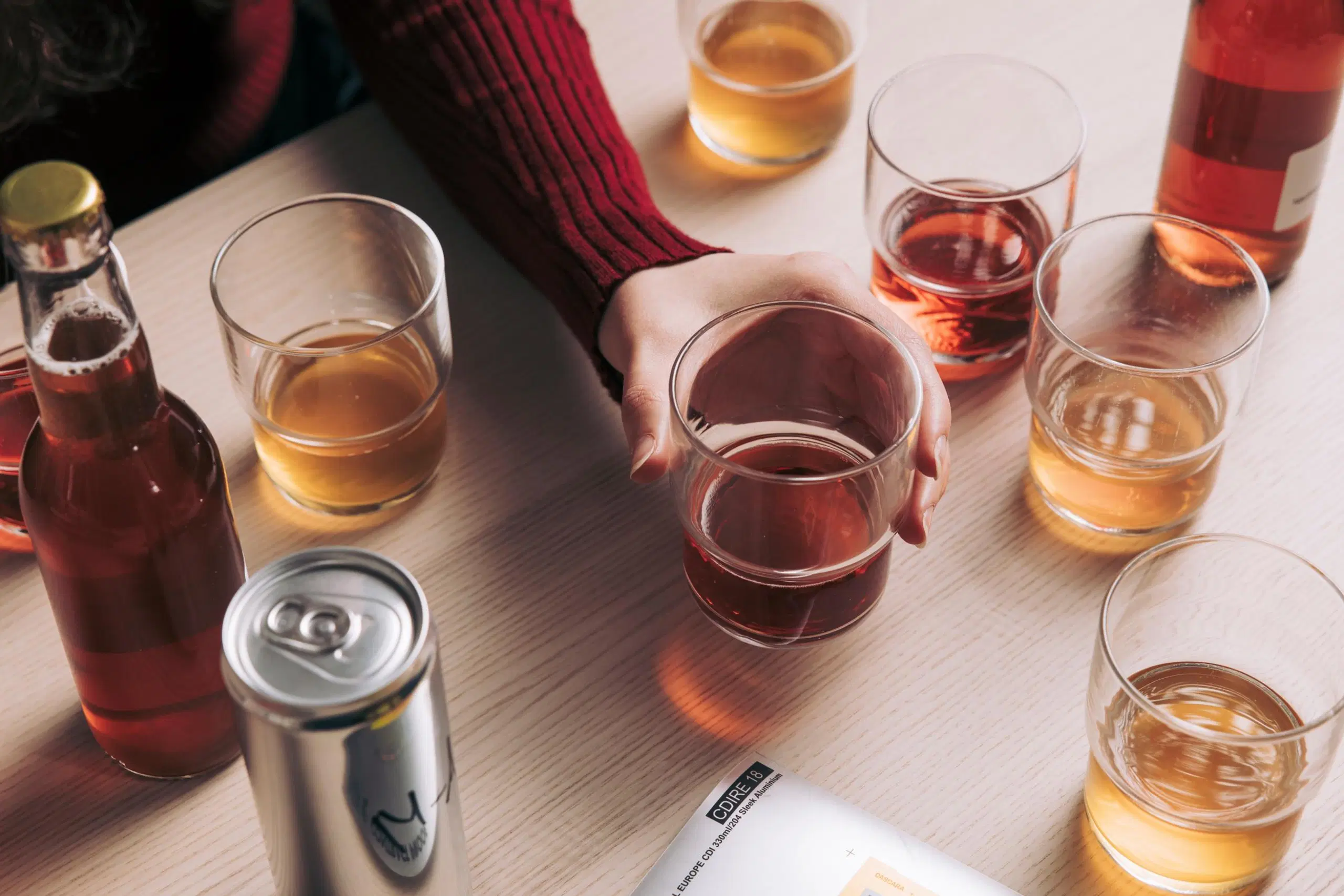 Laseja, joissa on vaaleaa ja punaruskeaa juomaa, kaksi lasipulloa ja juomatölkki