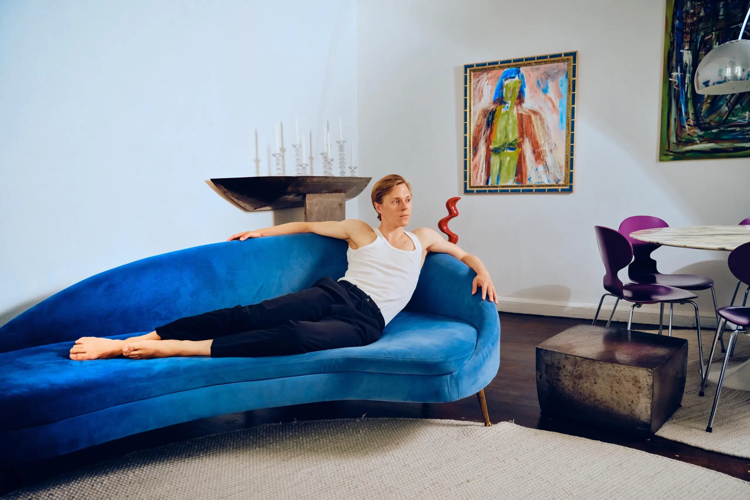 Atte Kilpinen makaa sinisellä samettisohvalla. Takana näkyy rautainen sivupöytä, jolla on kynttilöitä.