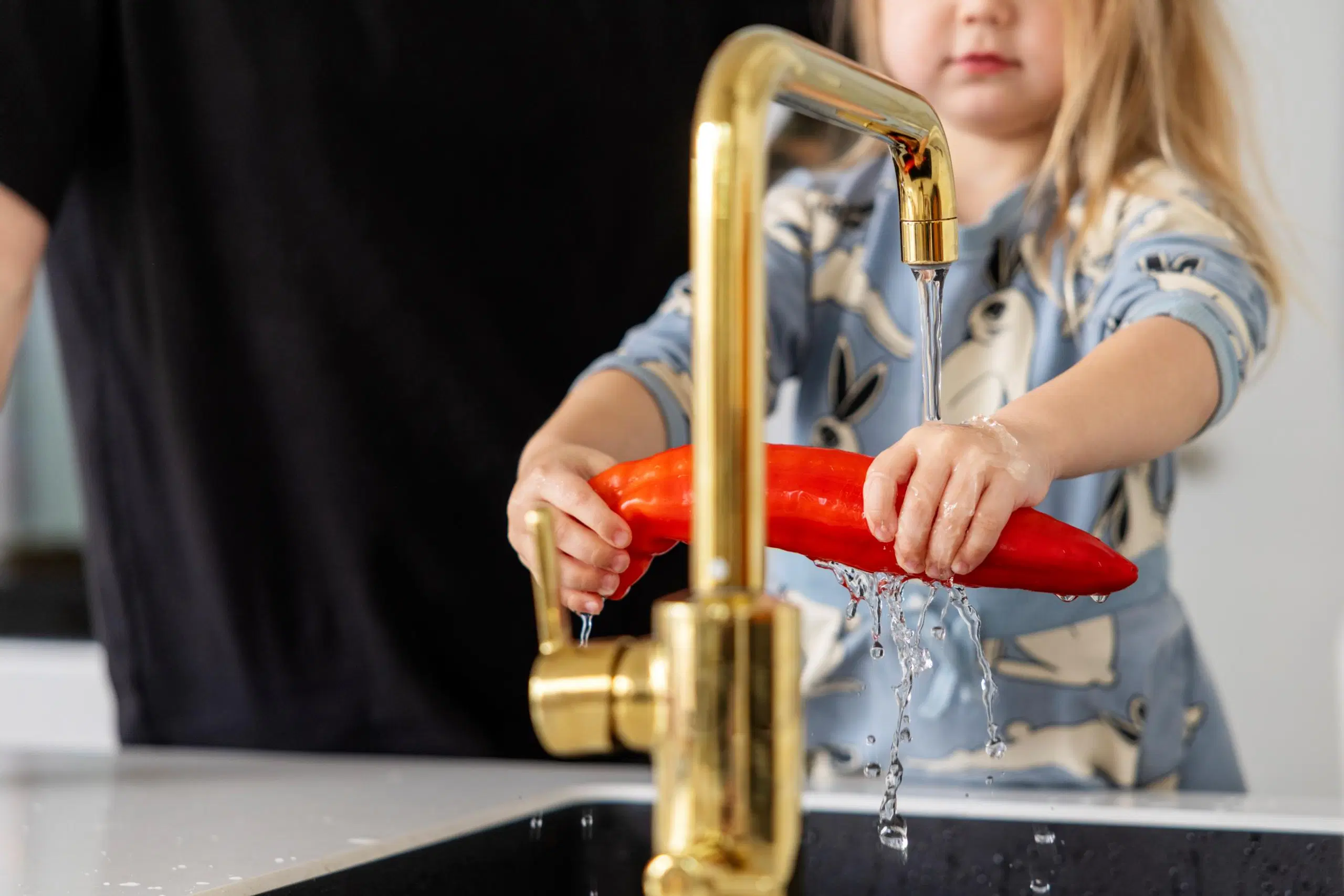 Lapsi pesee paprikaa vesihanan alla.