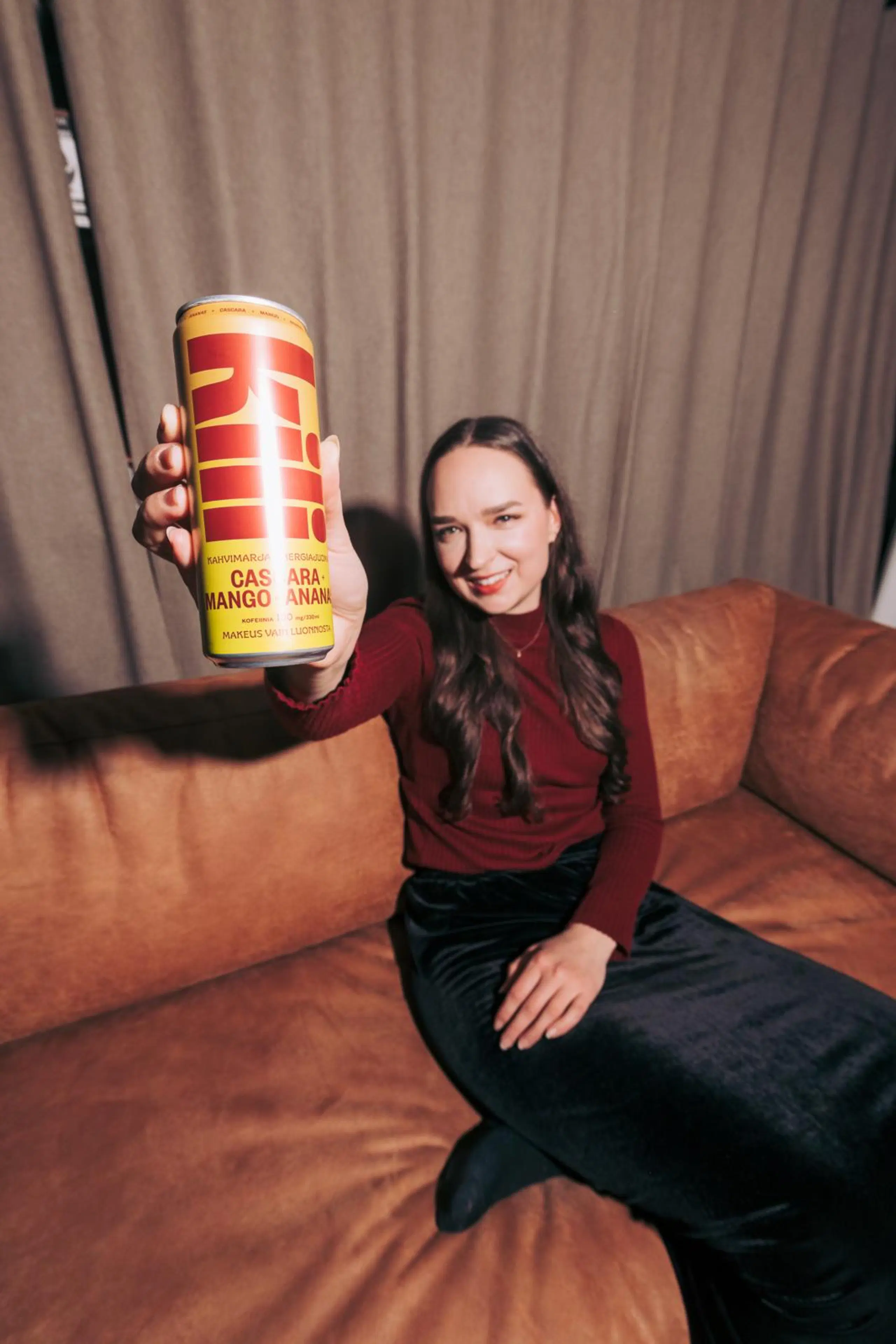 Anemone Aaltonen istuu sohvalla ja pitelee Kili-tölkkiä ylös ojennetussa kädessä