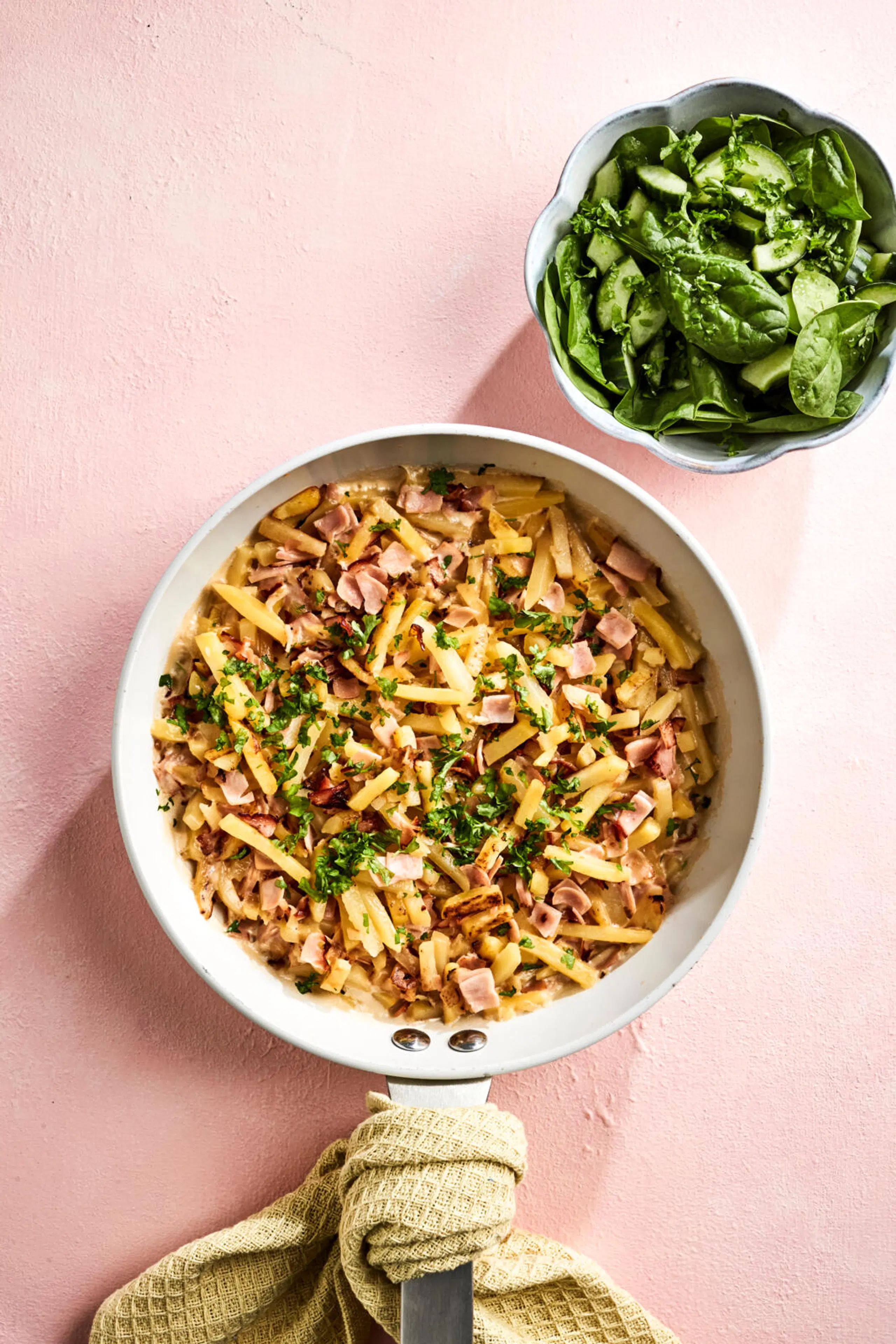 Paistinpannu täynnä peruna-kinkkupaistosta, jonka päällä persiljaa. Vieressä kulho vihreää salaattia.