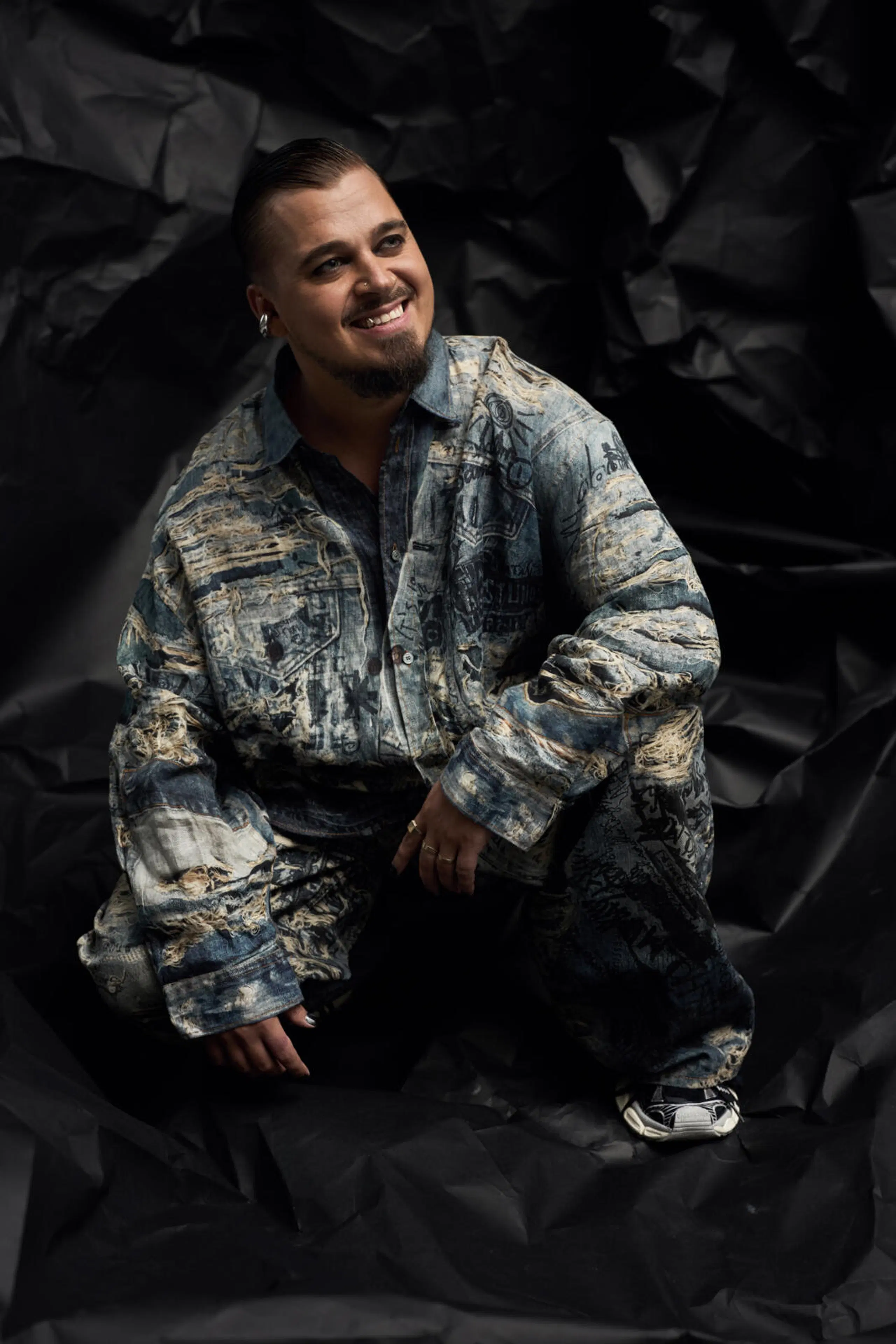 Hymyilevä Jere Pöyhönen kyykyssä mustan rypytetun taustakankaan edessä.