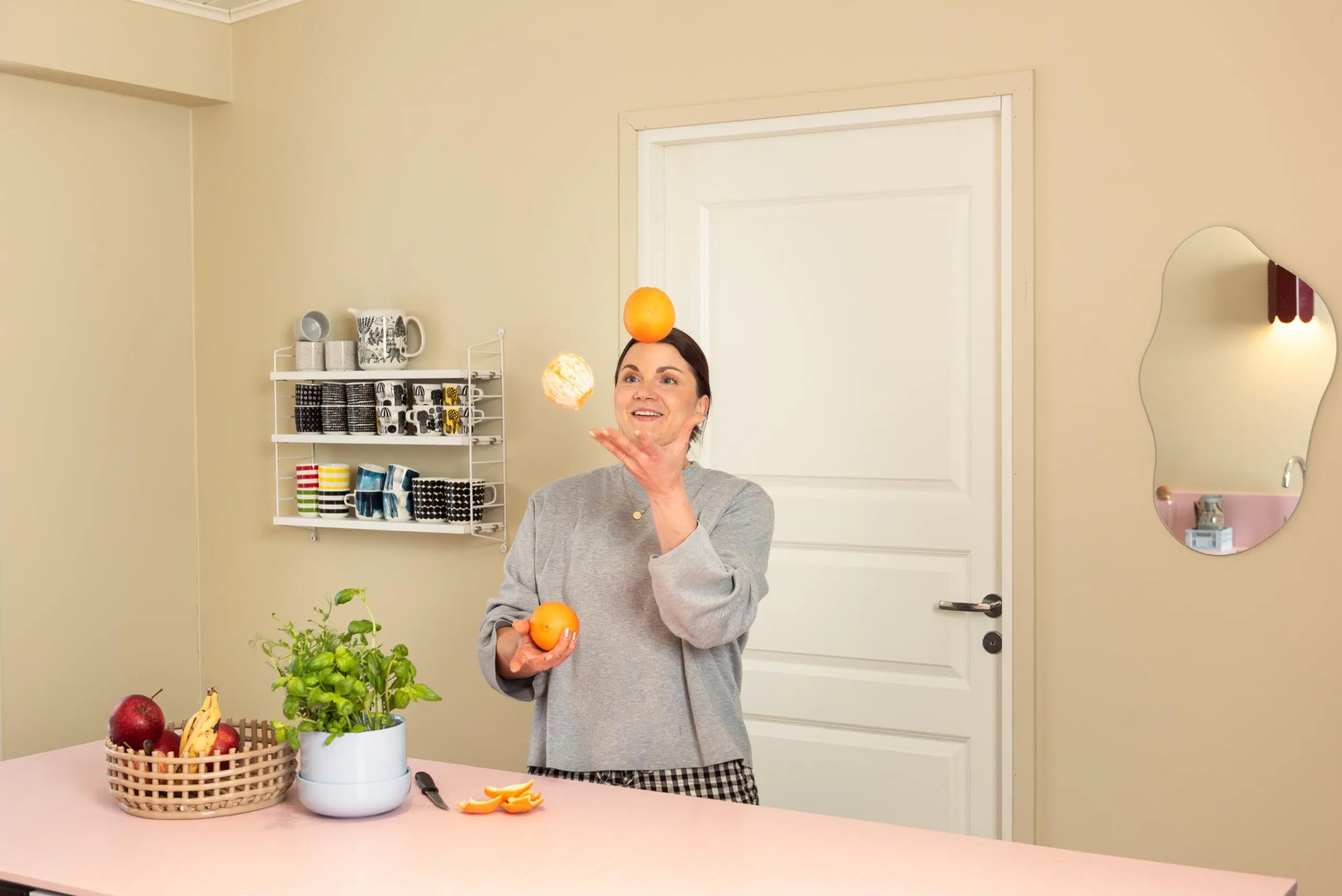 Maru Hautala jonglööraa appelsiineilla vaaleanpunaisen keittiösaarekkeen takana.