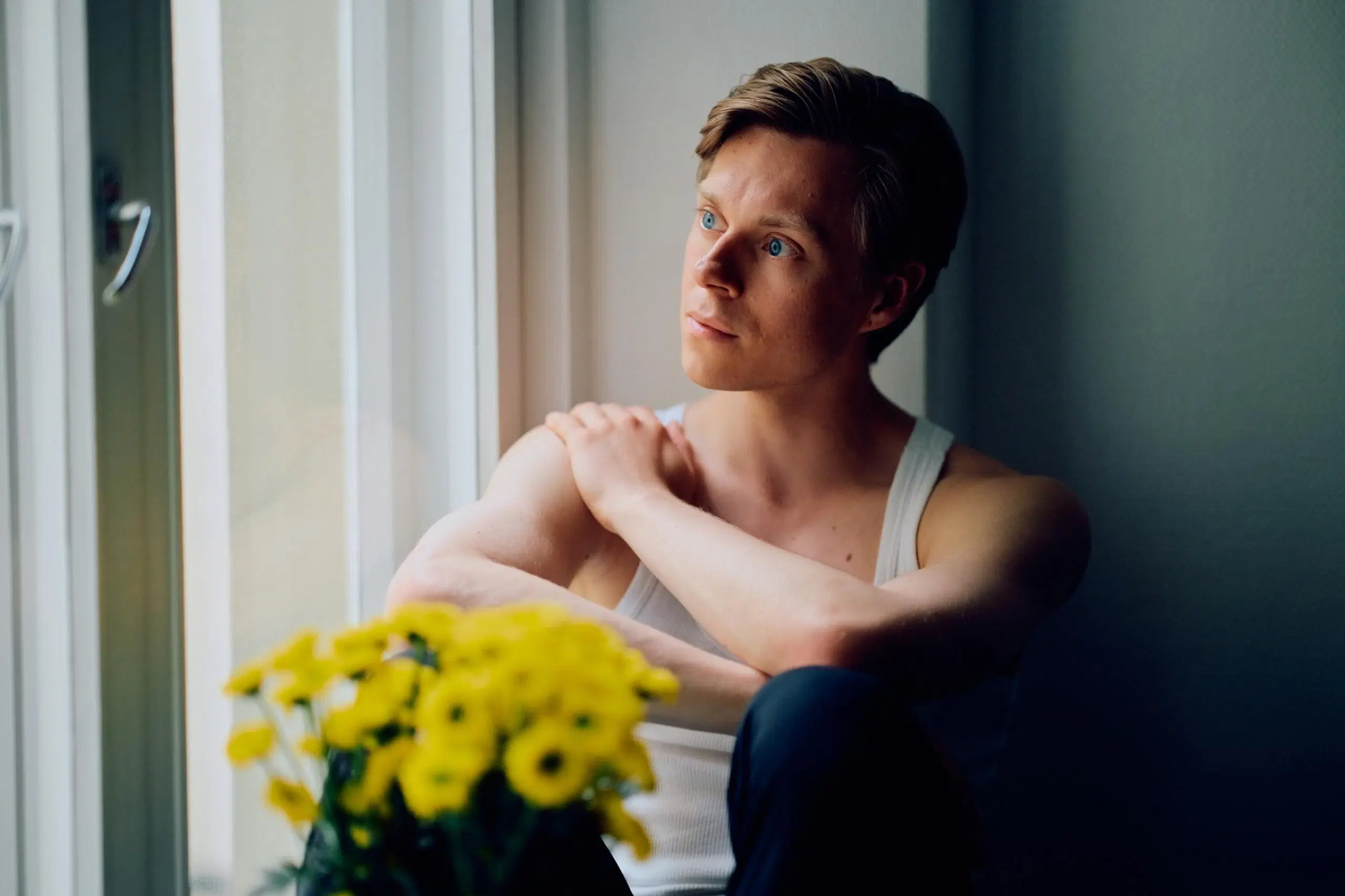 Atte Kilpinen katsoo ulos ikkunasta. Hänen edessään on kimppu keltaisia kukkia.