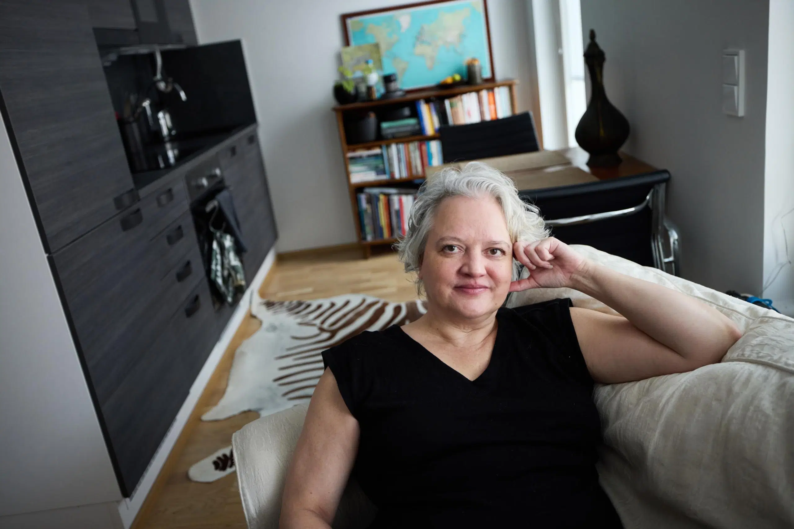Tanja Mikkola etualalla nojatuolissa, taustalla näkyy kirjahylly ja keittiö.