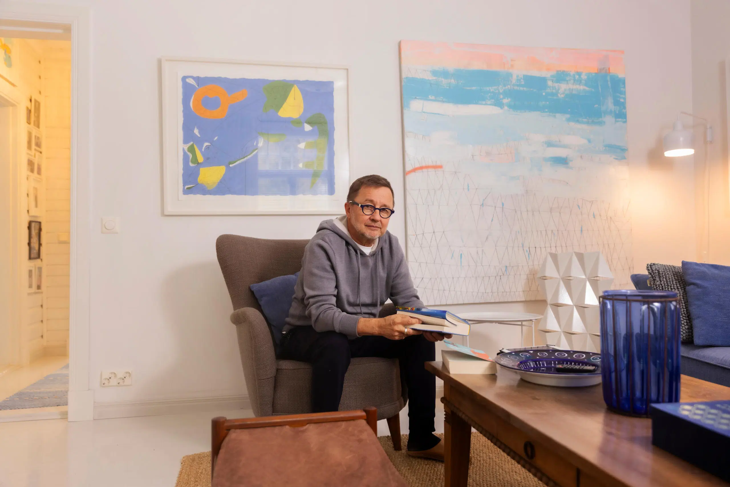 Matti Remes olohuoneessa. Seinällä taidetta ja olohuoneen pöydällä sinistä lasia.